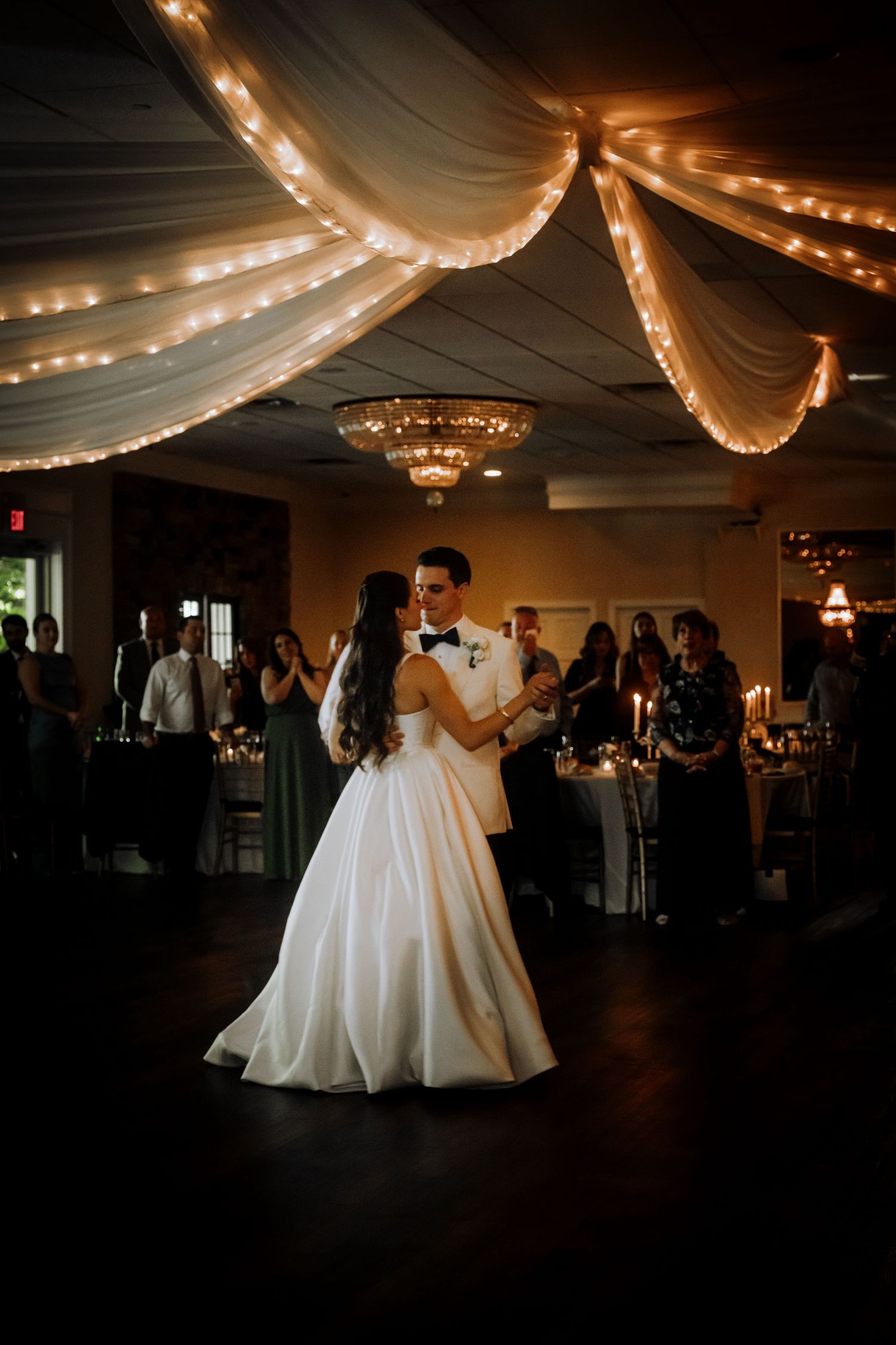 First dance under romantic draped fabric and string lights at an elegant wedding reception.