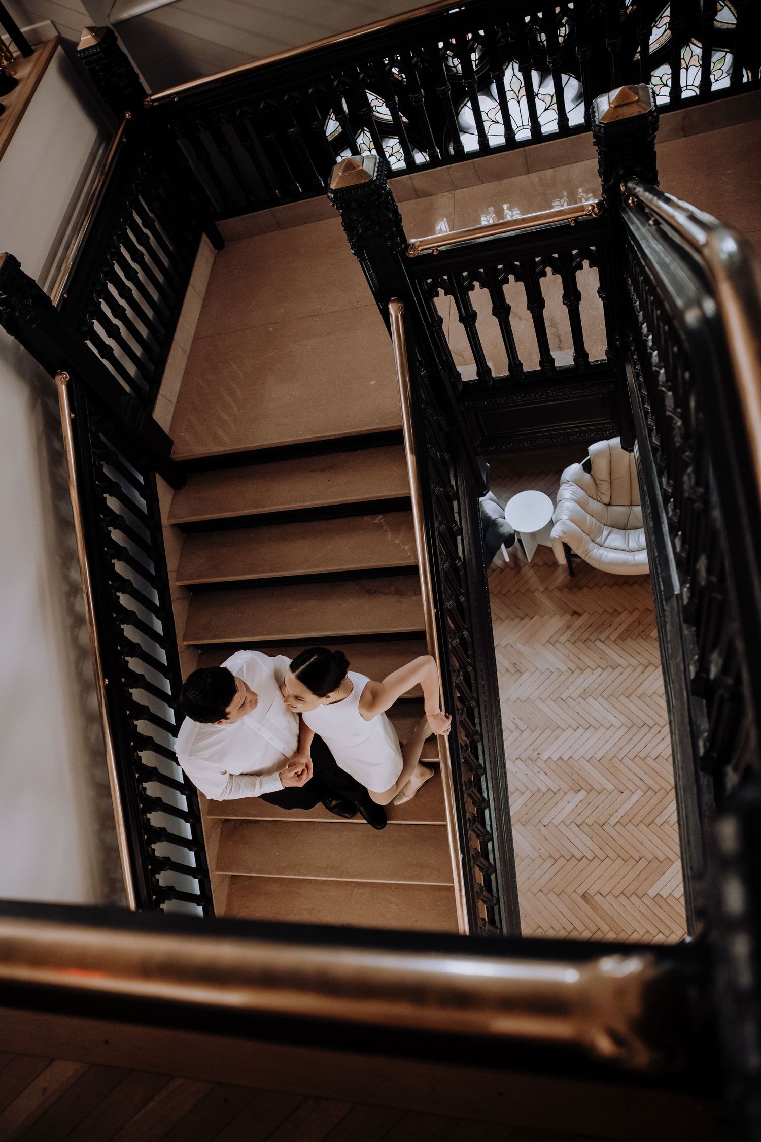 Overhead view of couple on wooden staircase with ornate black railings.