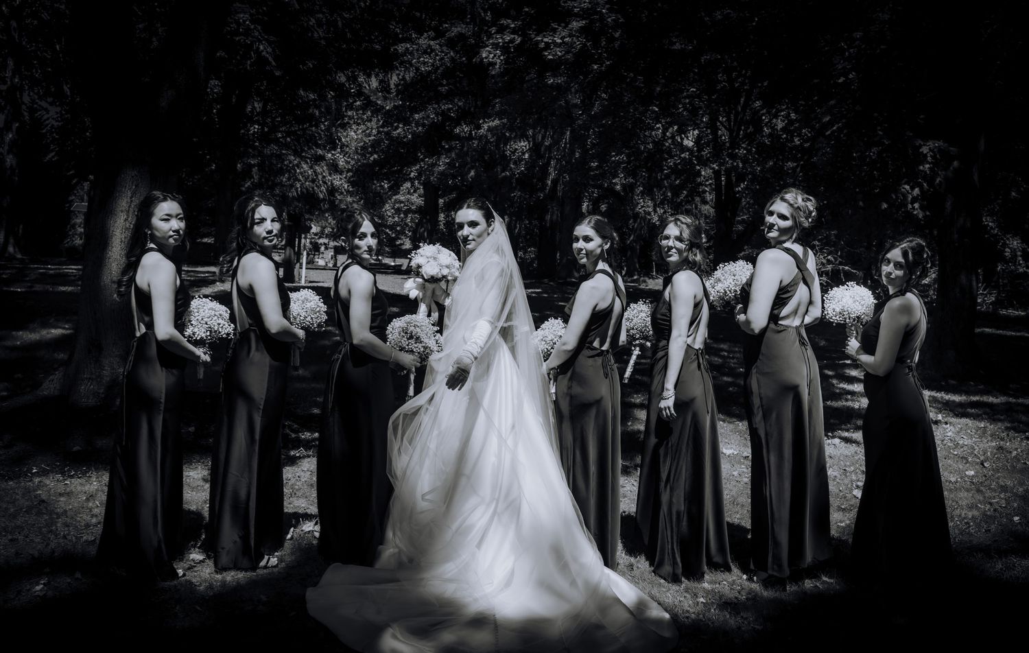 Wedding party in black and white dresses poses together in outdoor garden setting.Editorial and Cinematic Wedding photos