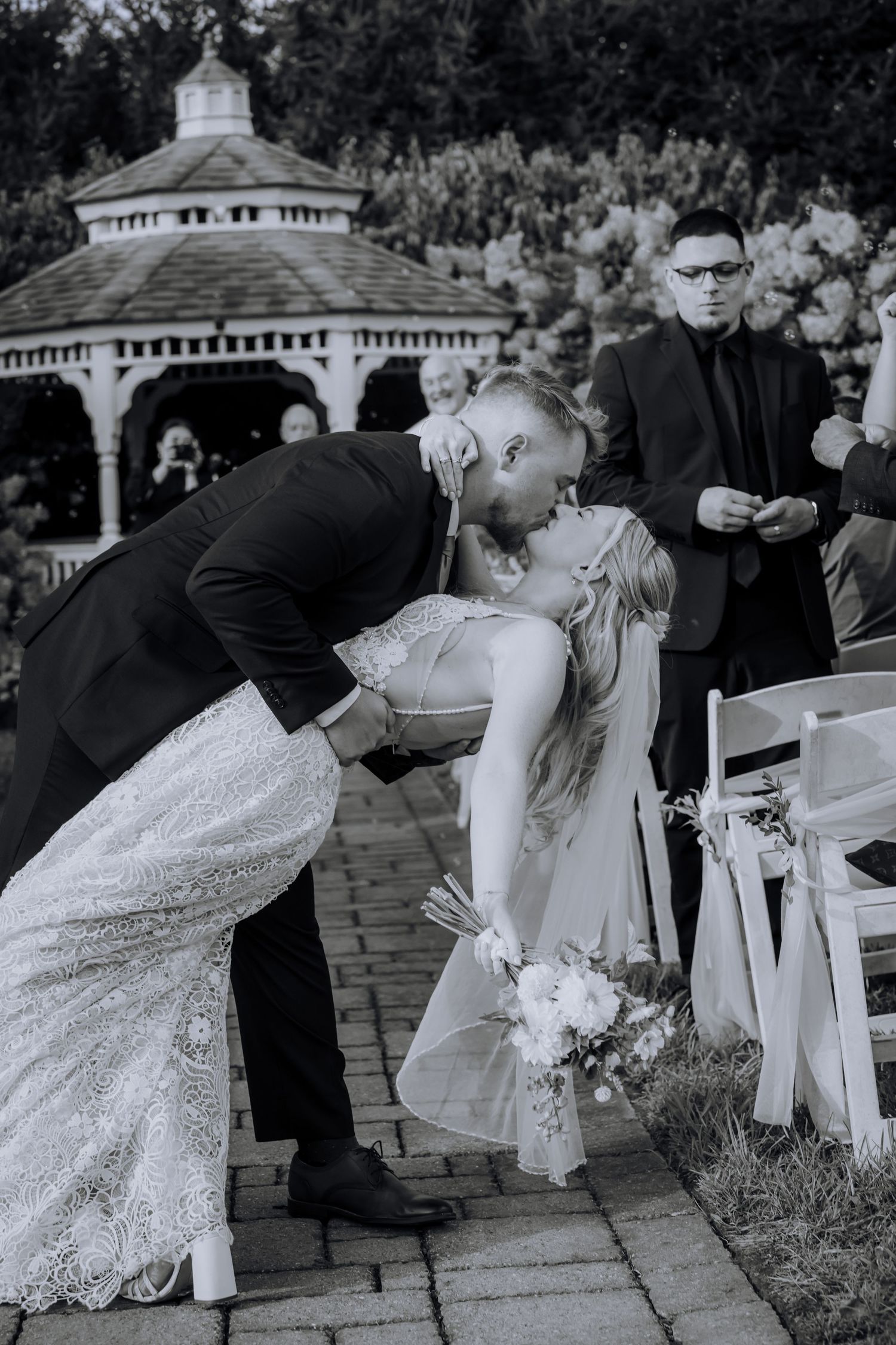 Black and white photo of a couple sharing a romantic dip kiss in front of a gazebo.Editorial and Cinematic Wedding photos