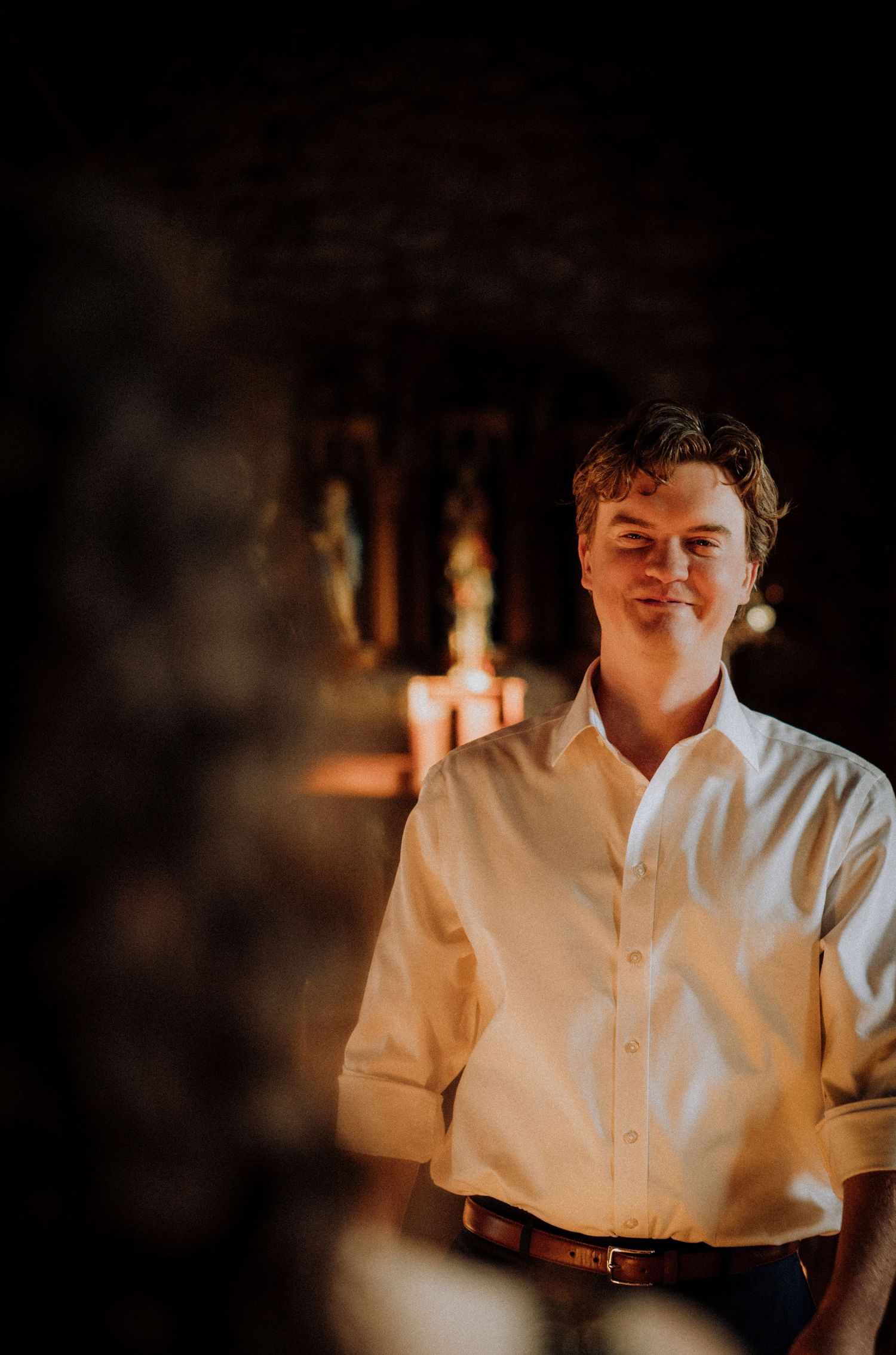 A dimly lit portrait in warm tones showing someone wearing a white button-up shirt.