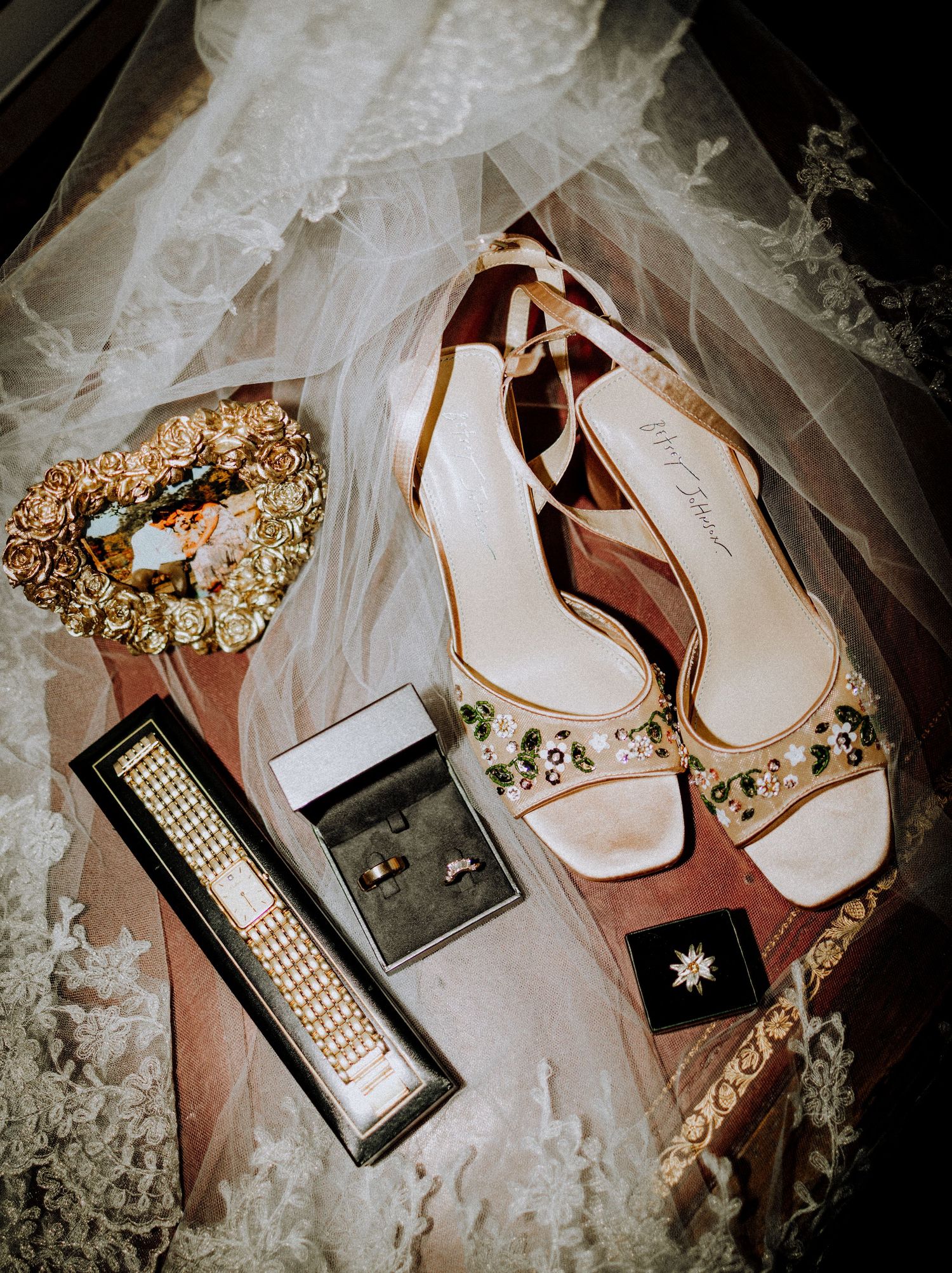 Elegant bridal flat lay featuring embellished heels, diamond bracelet, rings, floral crown, and lace veil on a soft background.