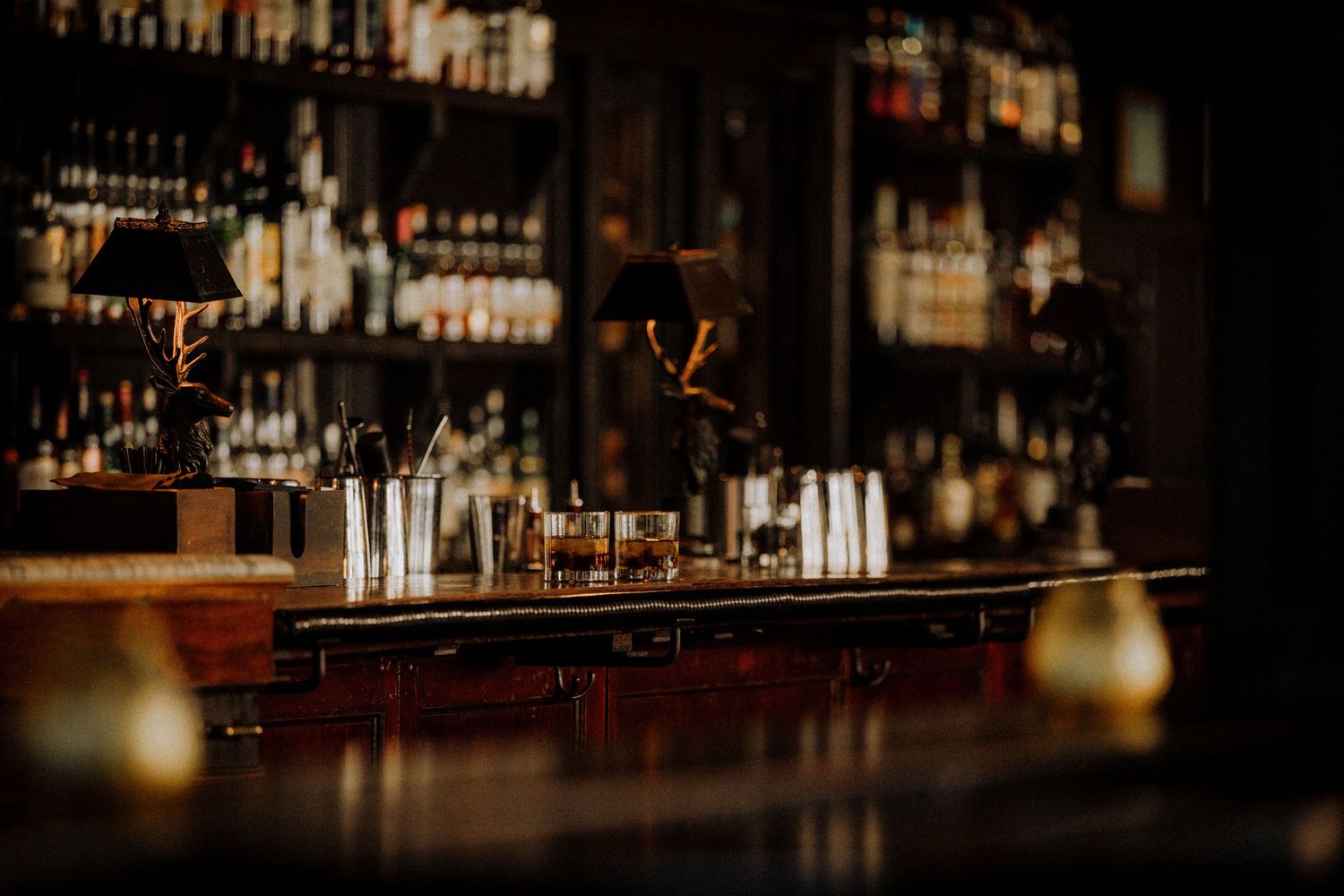 Dimly lit upscale bar los-angeles-wedding-photographerwhiskey glasses, bottles on shelves, and warm golden accents in elegant dark ambiance.