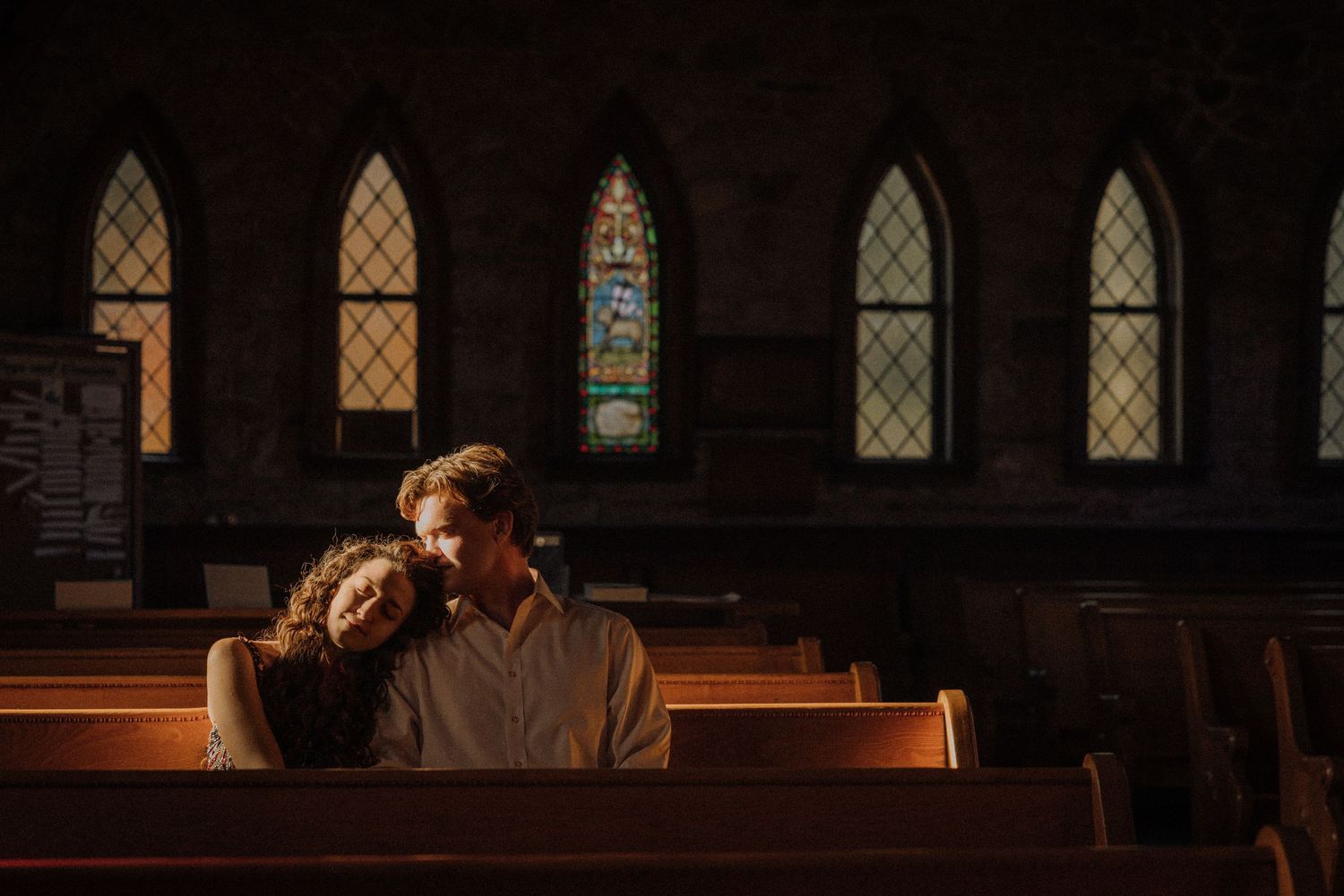 Stained glass windows cast colorful light in historic church sanctuary.