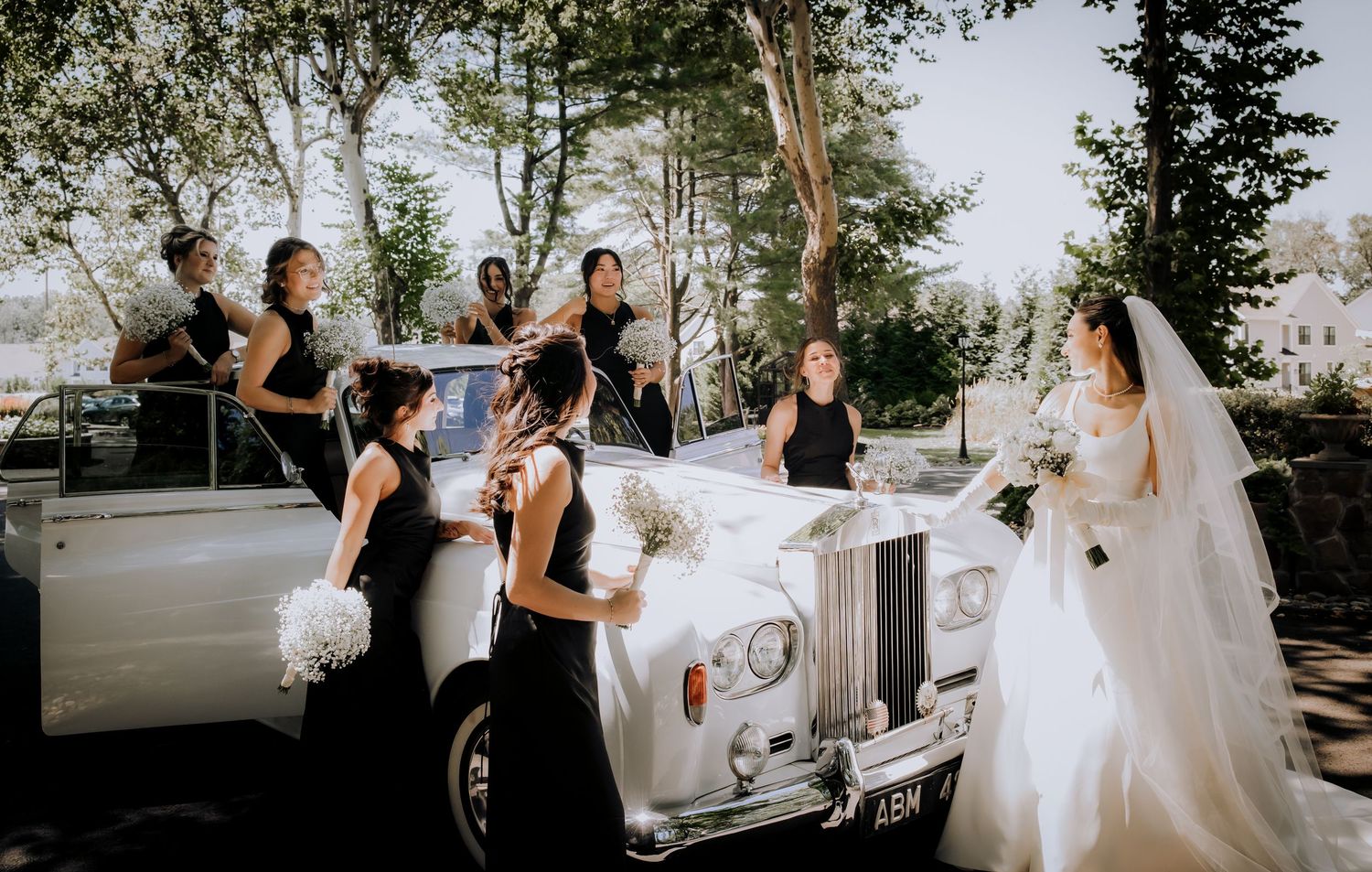 Wedding party poses with a classic white Rolls Royce decorated with floral arrangements.