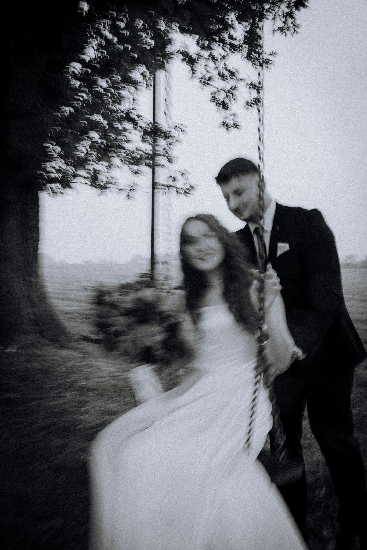 Motion-blurred artistic black and white photo of newlyweds on a swing.