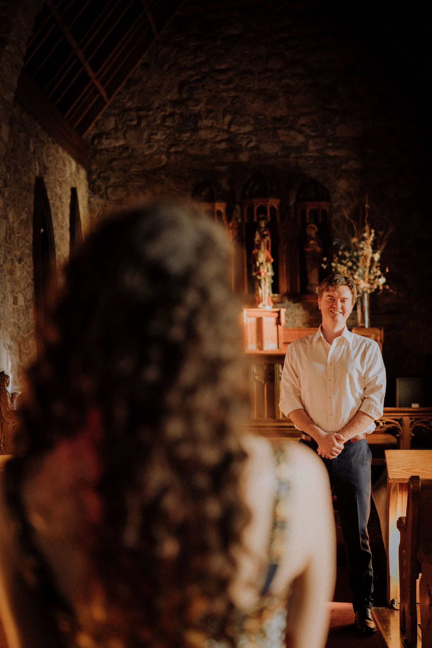 A romantic moment captured in a stone church with dramatic lighting and shadows.