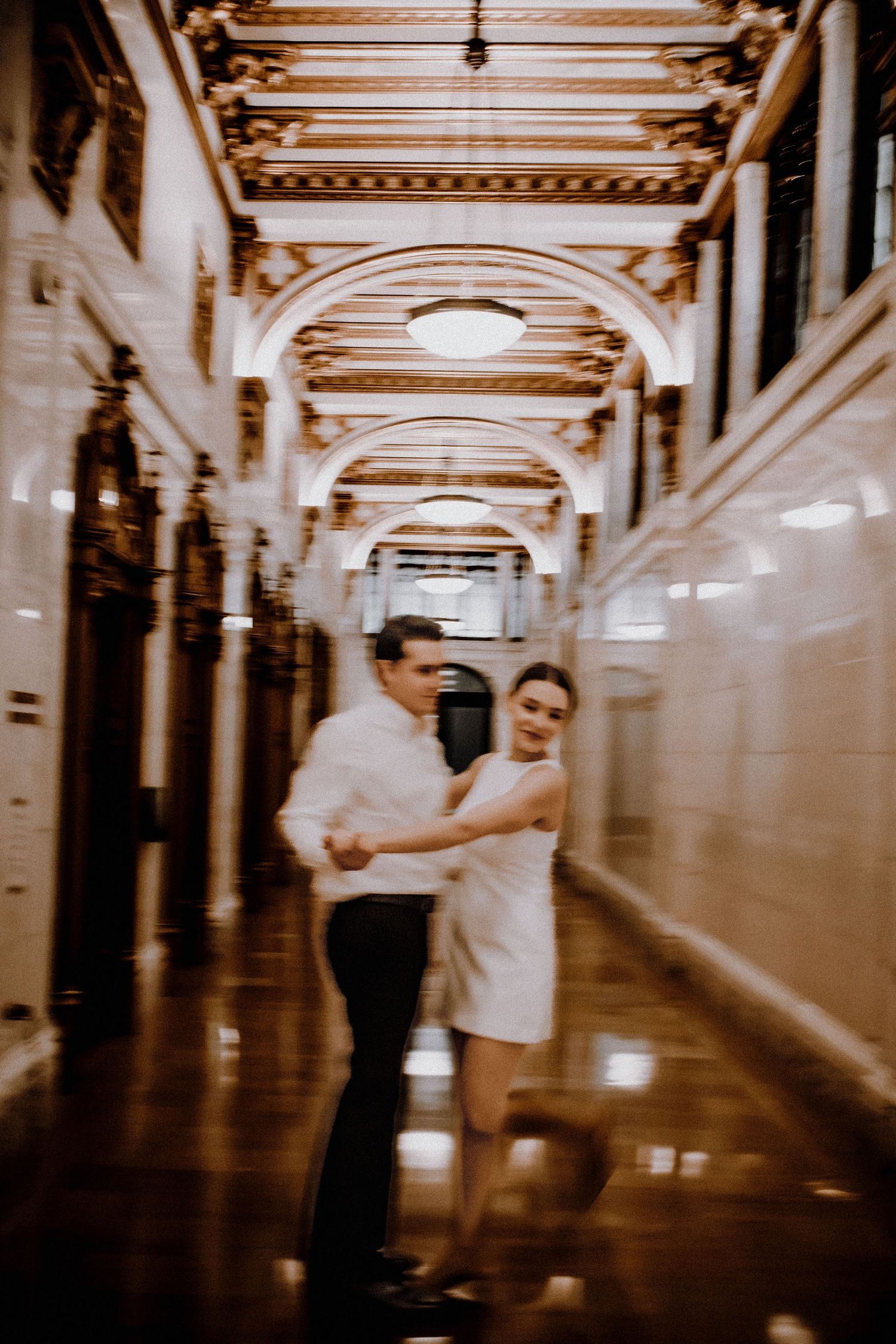 Couple dancing in an elegant hallway with ornate architectural details and arched ceilings.