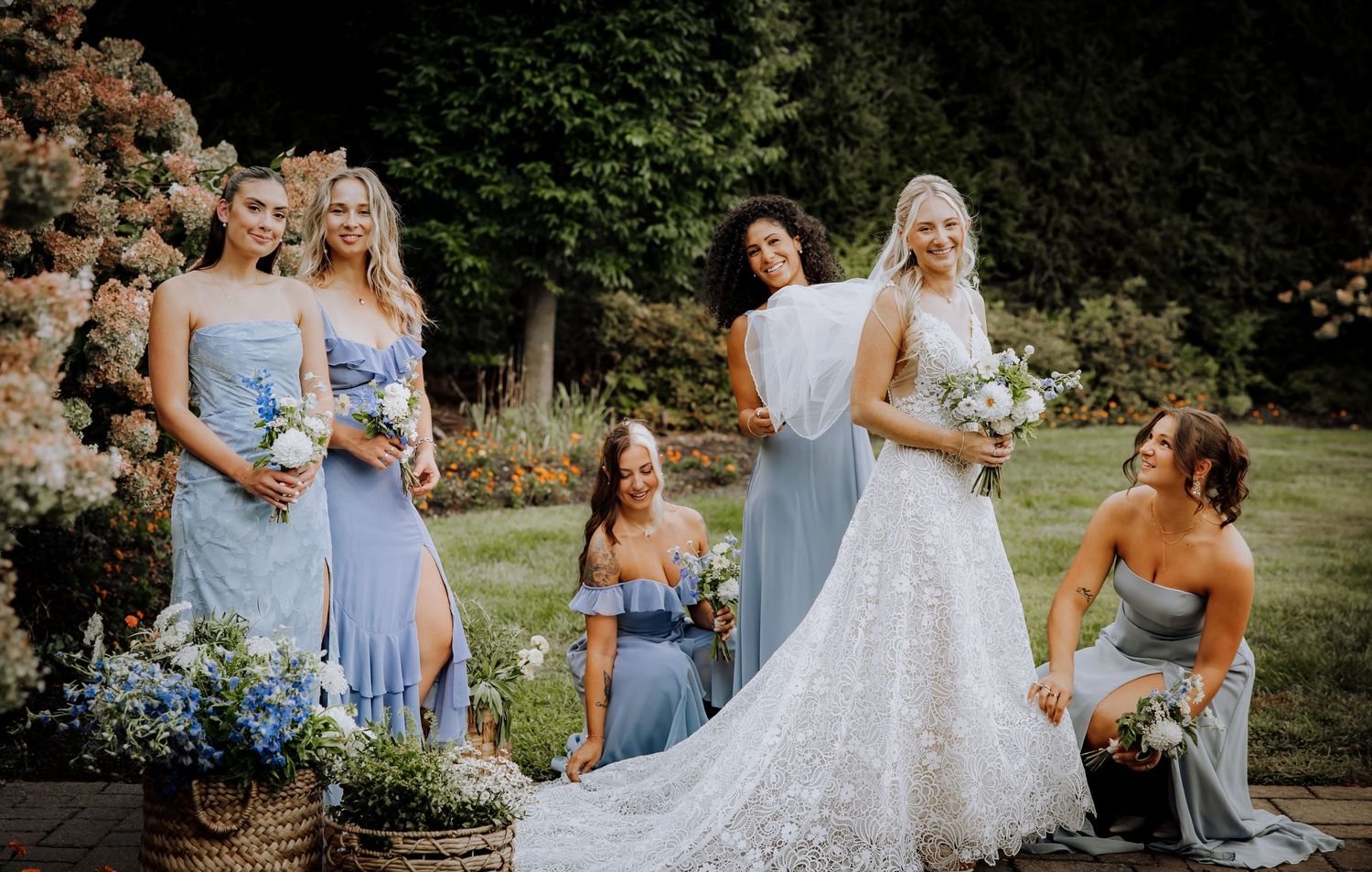 Wedding party in light blue bridesmaid dresses posing outdoors with the bride in white.