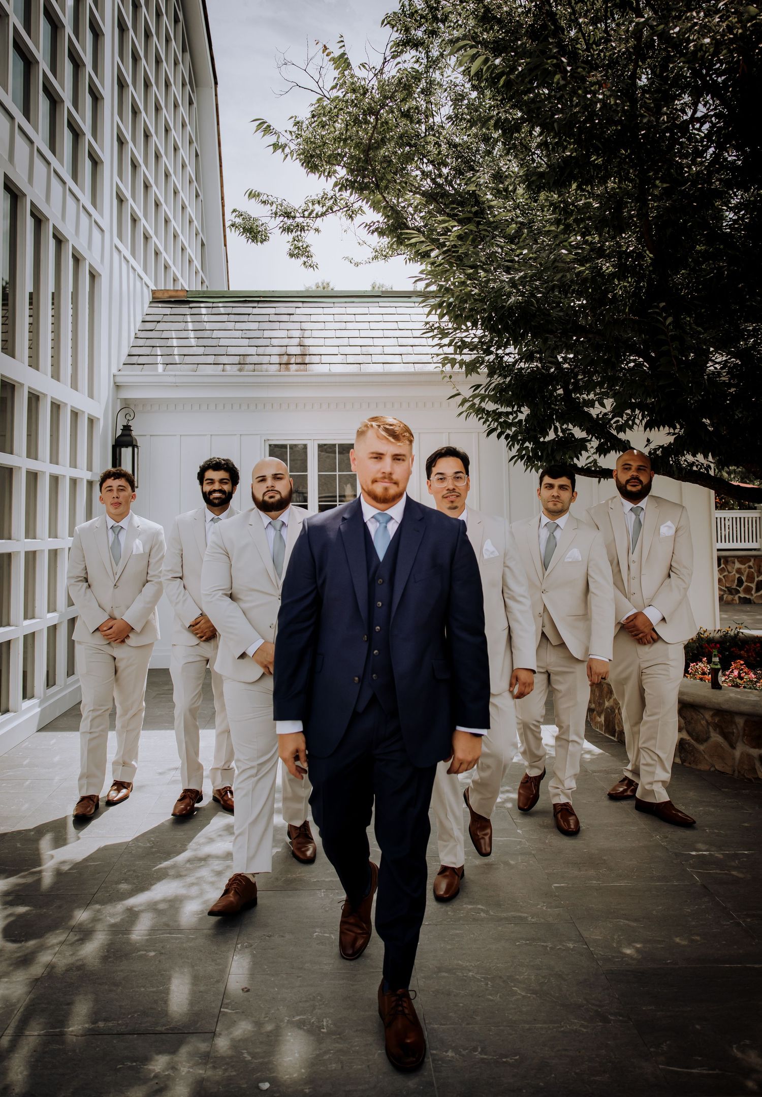 Groom in navy suit walking confidently with groomsmen in light suits behind him.Editorial and Cinematic Wedding photos