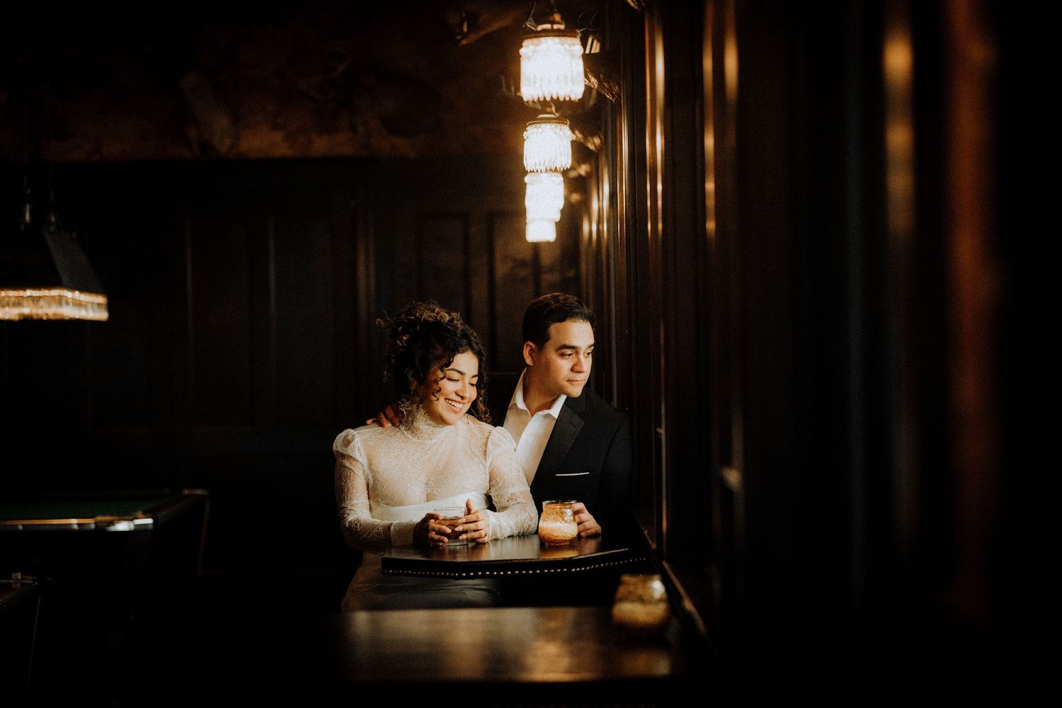 seven-grand-engagement-photoElegant couple sharing a romantic moment at a dimly lit bar, dressed in formal attire for a wedding celebration.
