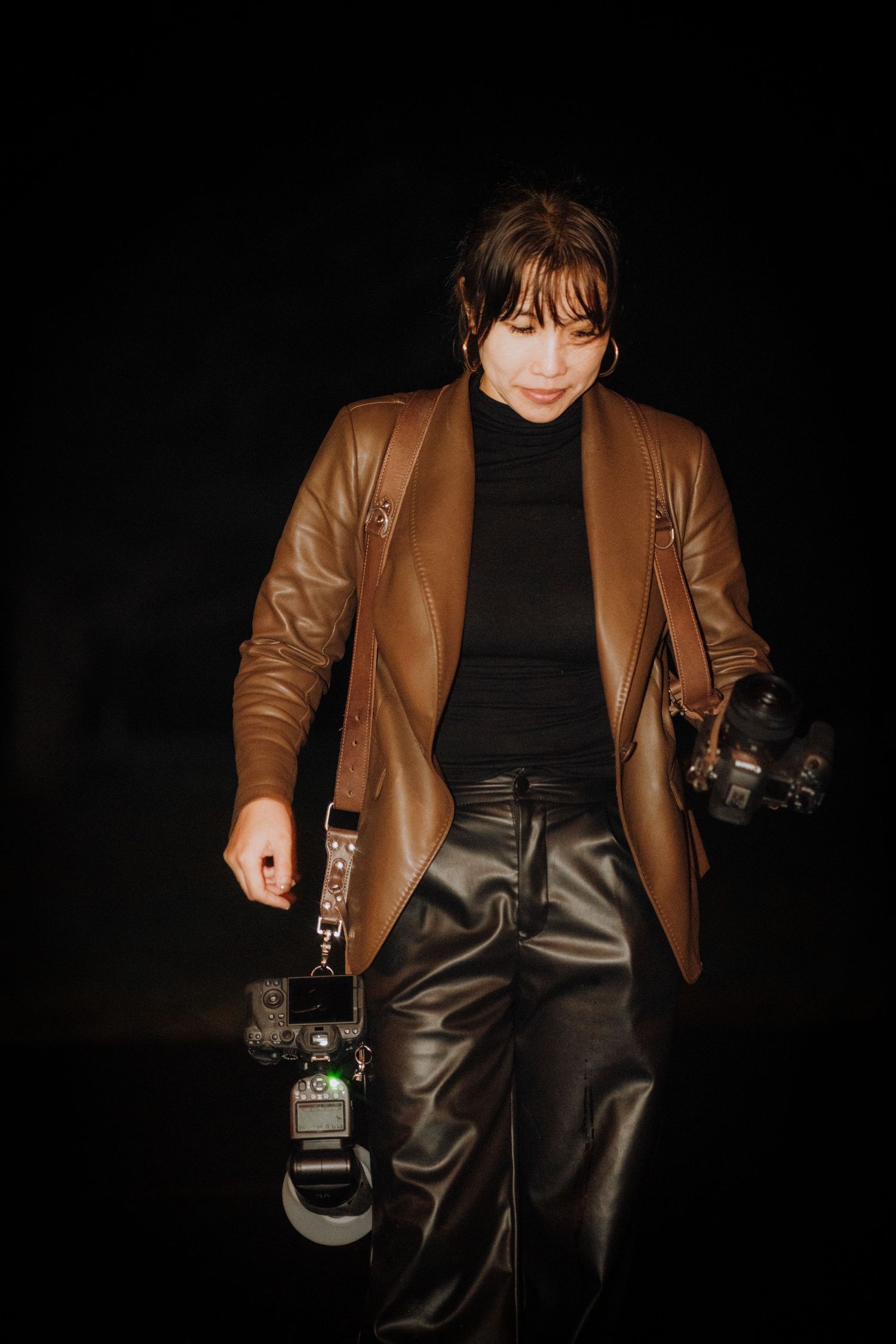 A stylish brown leather jacket and black outfit photographed against a dark background.