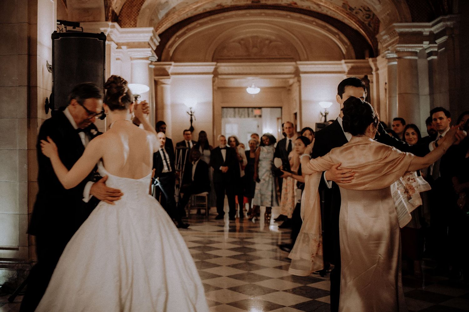 Elegant wedding first dance in ornate ballroom with guests watching the couple in formal attire.