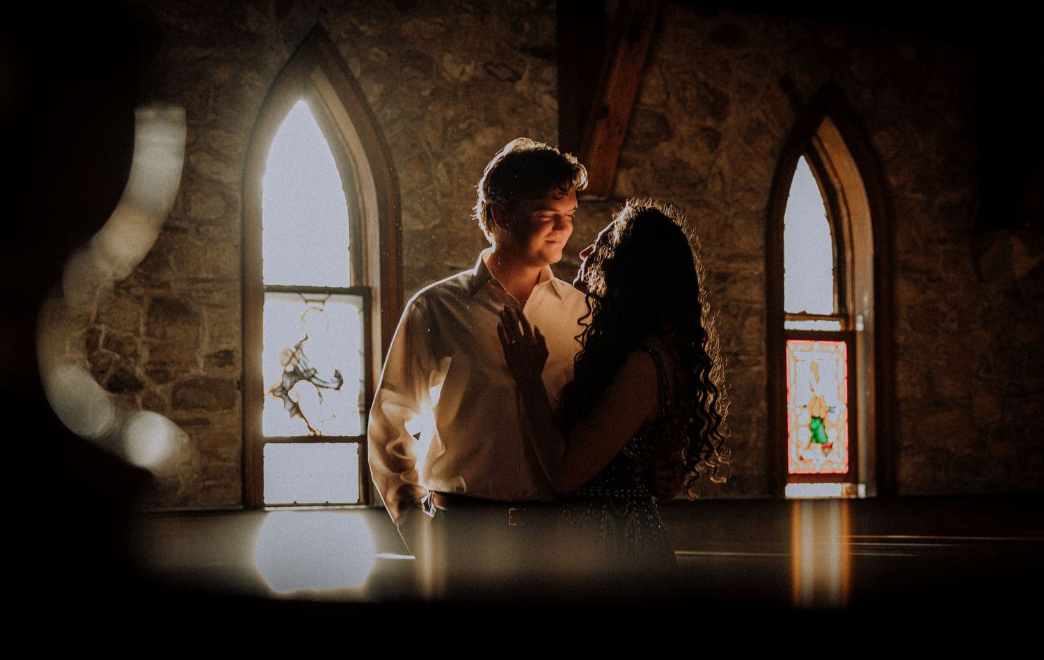 A couple embracing in front of gothic church windows with dramatic lighting.