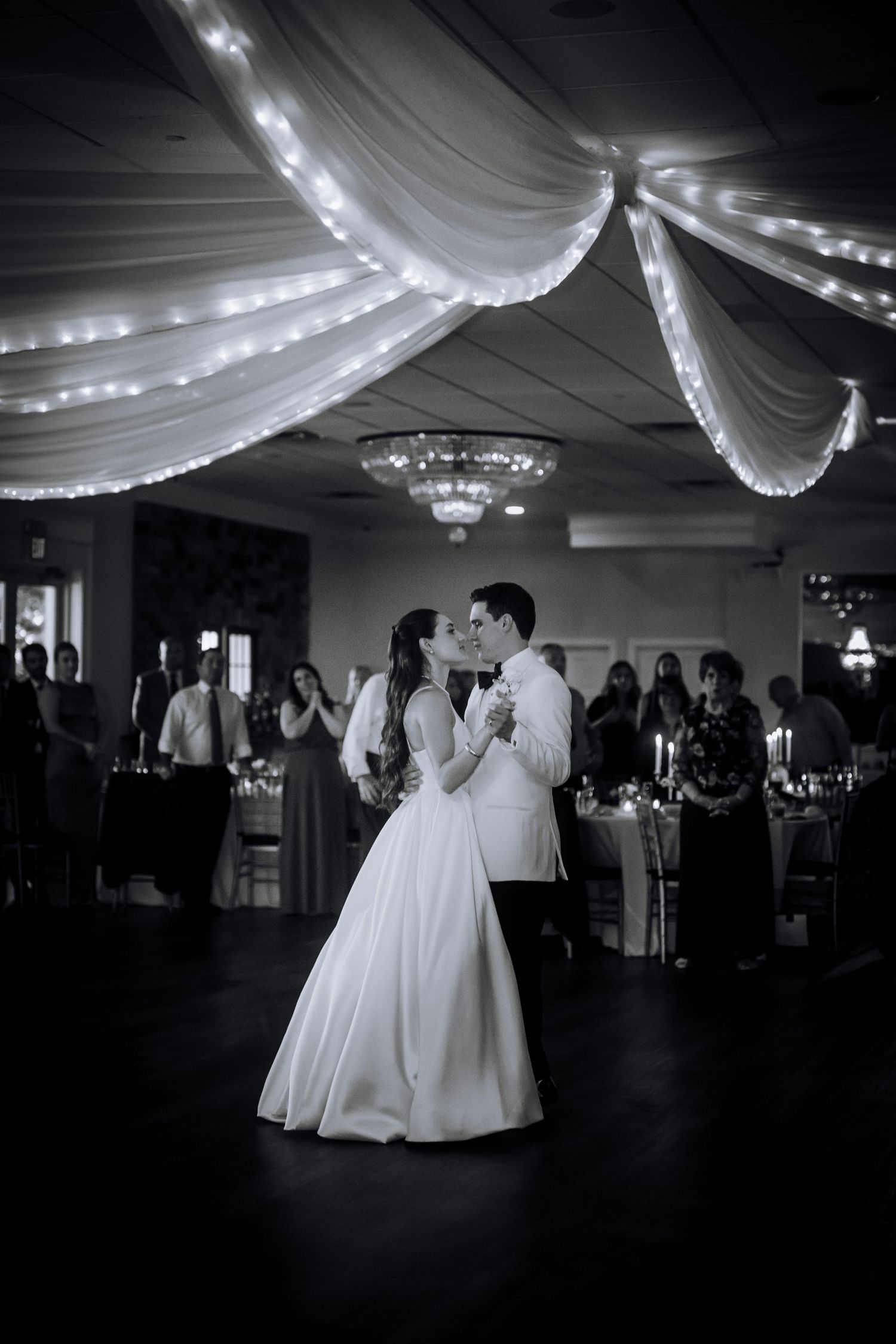 Elegant ballroom wedding reception with white fabric draping and string lights on the ceiling.