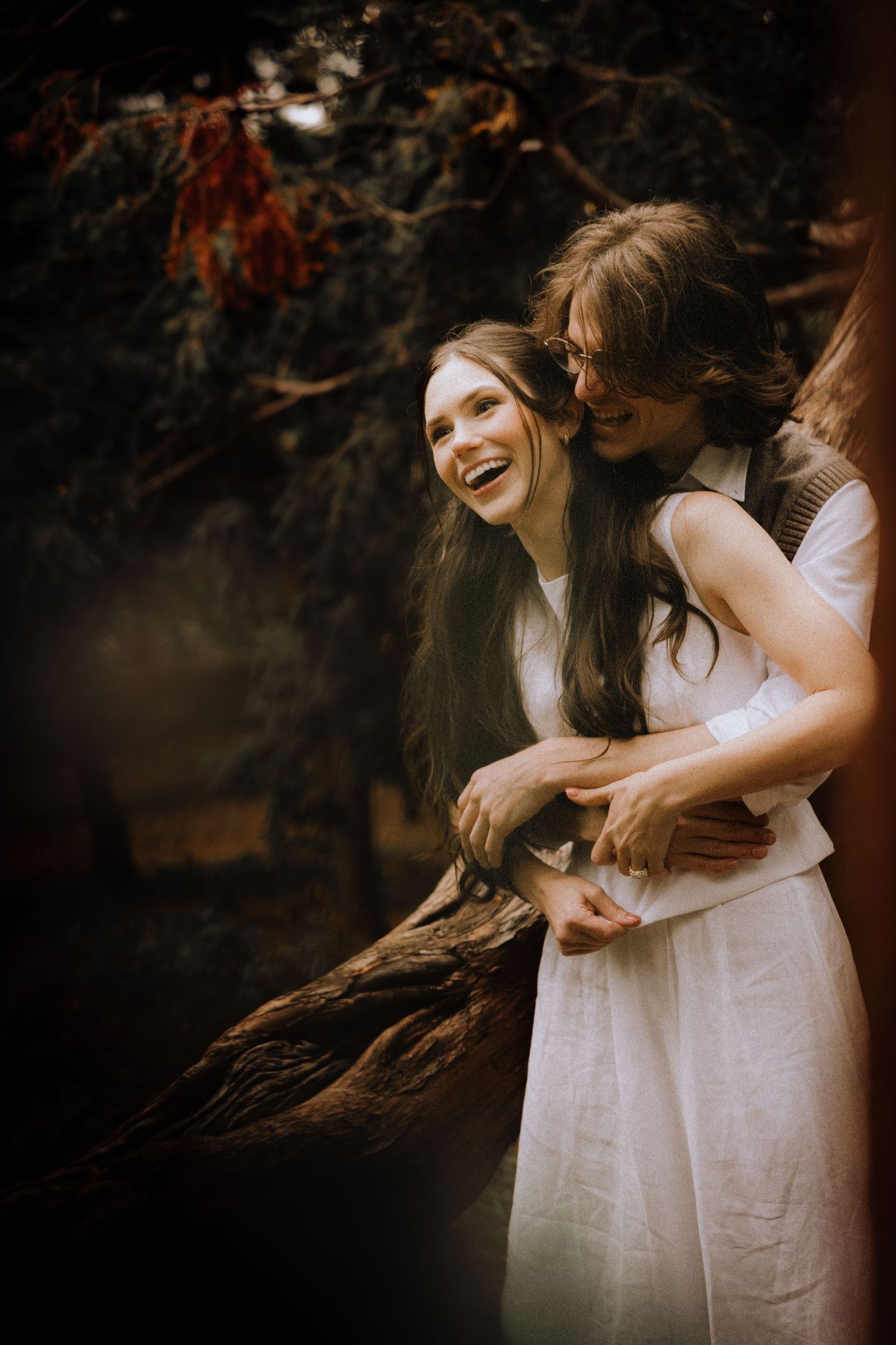 Two people in white dresses share a joyful embrace outdoors.