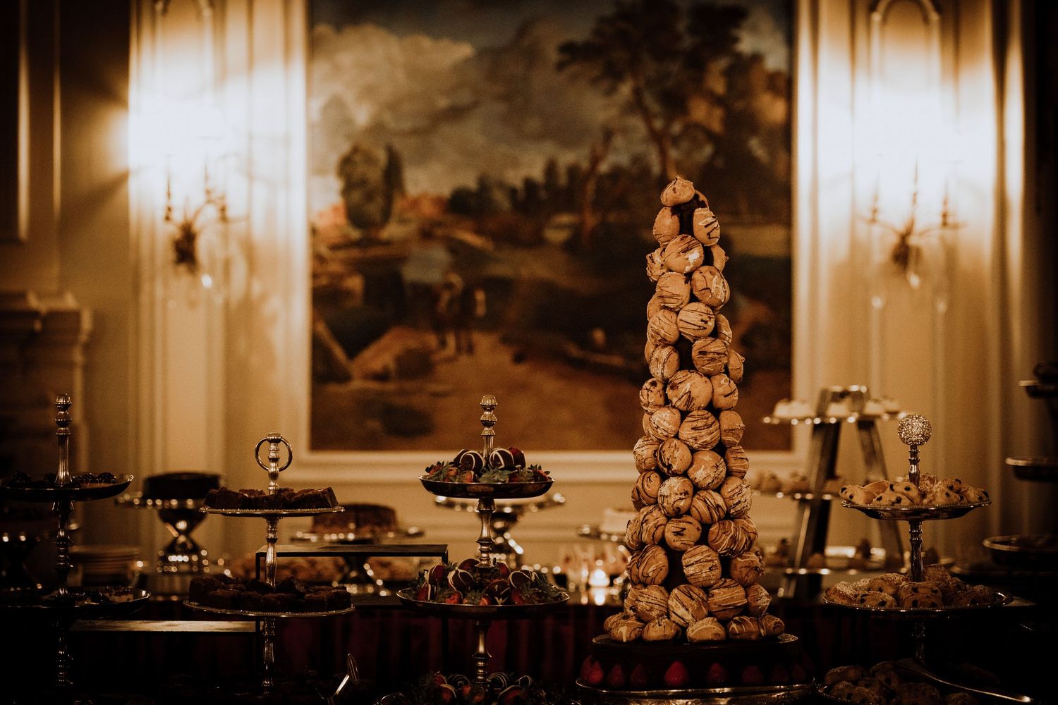 Elegant croquembouche tower centerpiece on a dessert table with silver stands in a grand candlelit ballroom.