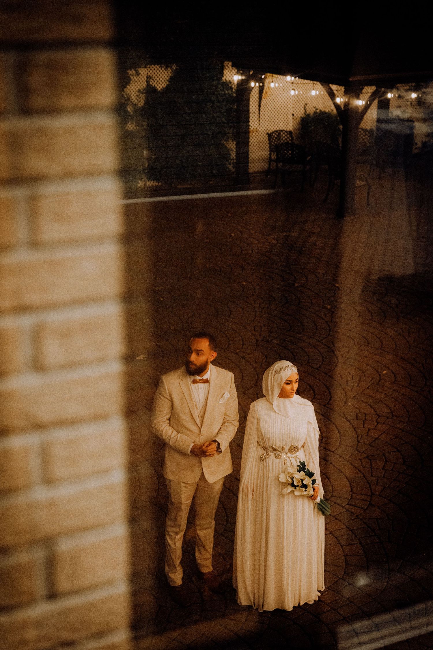Wedding couple in white attire photographed in an intimate indoor setting with warm lighting.