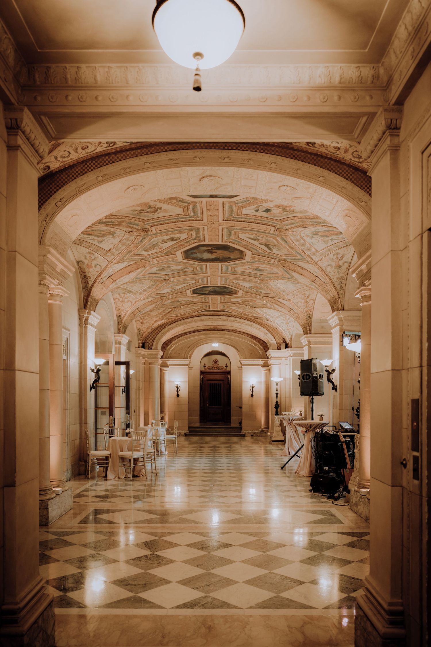 Grand neoclassical hallway with ornate arched ceilings, marble floors, and elegant event setup in warm ambient lighting.