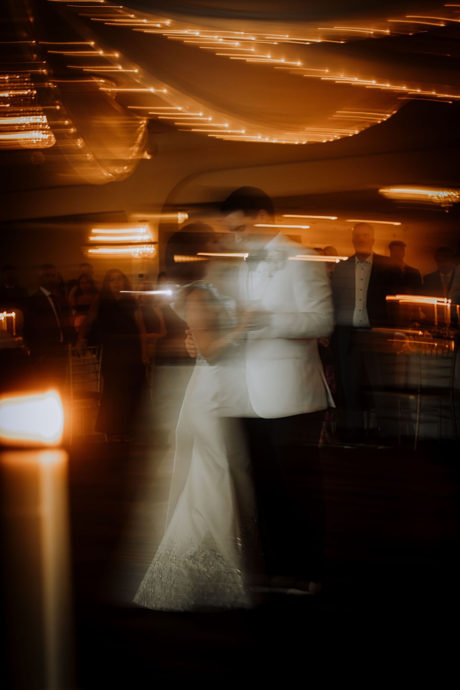 Long exposure photo creates ghostly motion blur effect of a wedding dress in warm lighting.