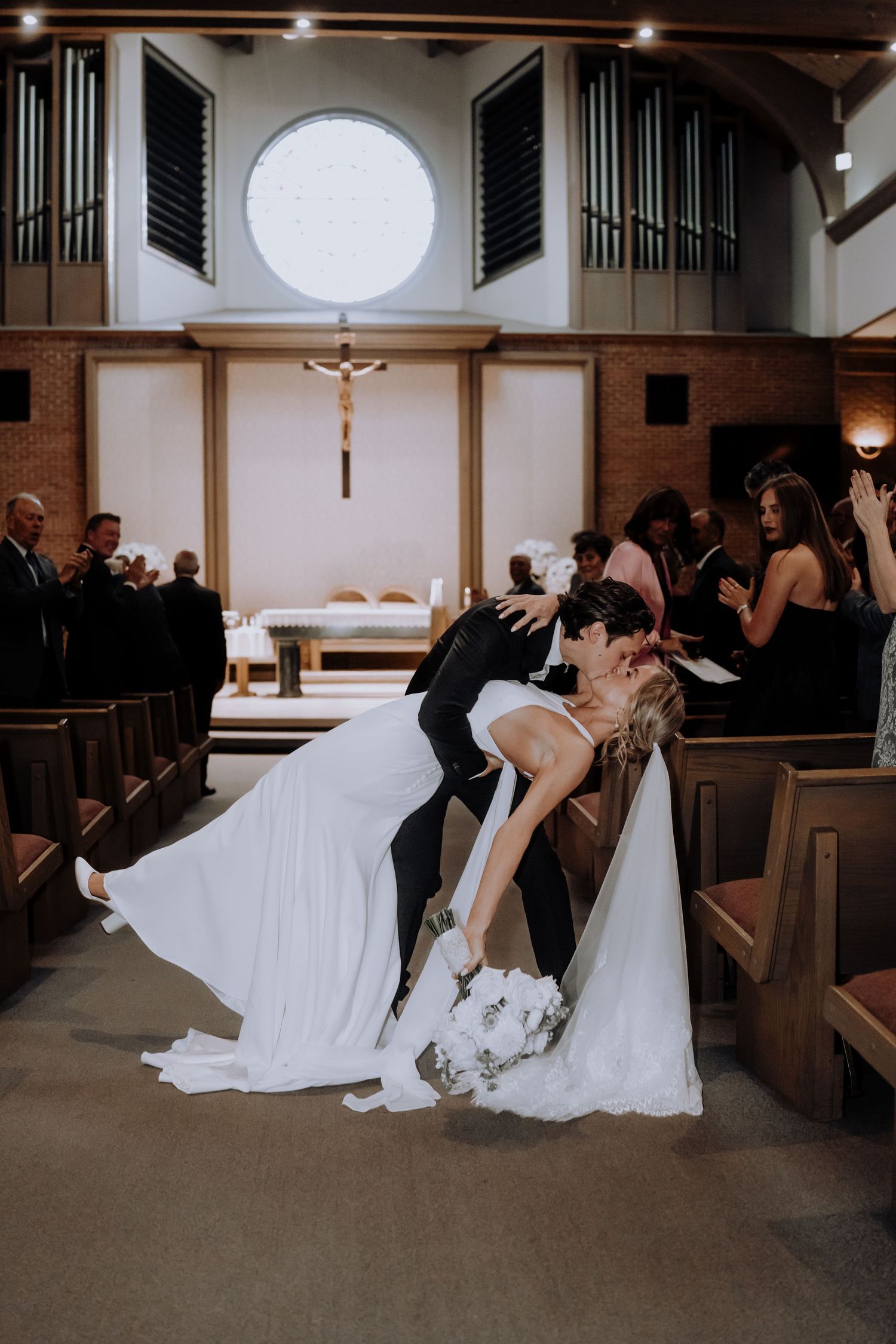 Wedding couple reclining across church pews during an intimate moment.