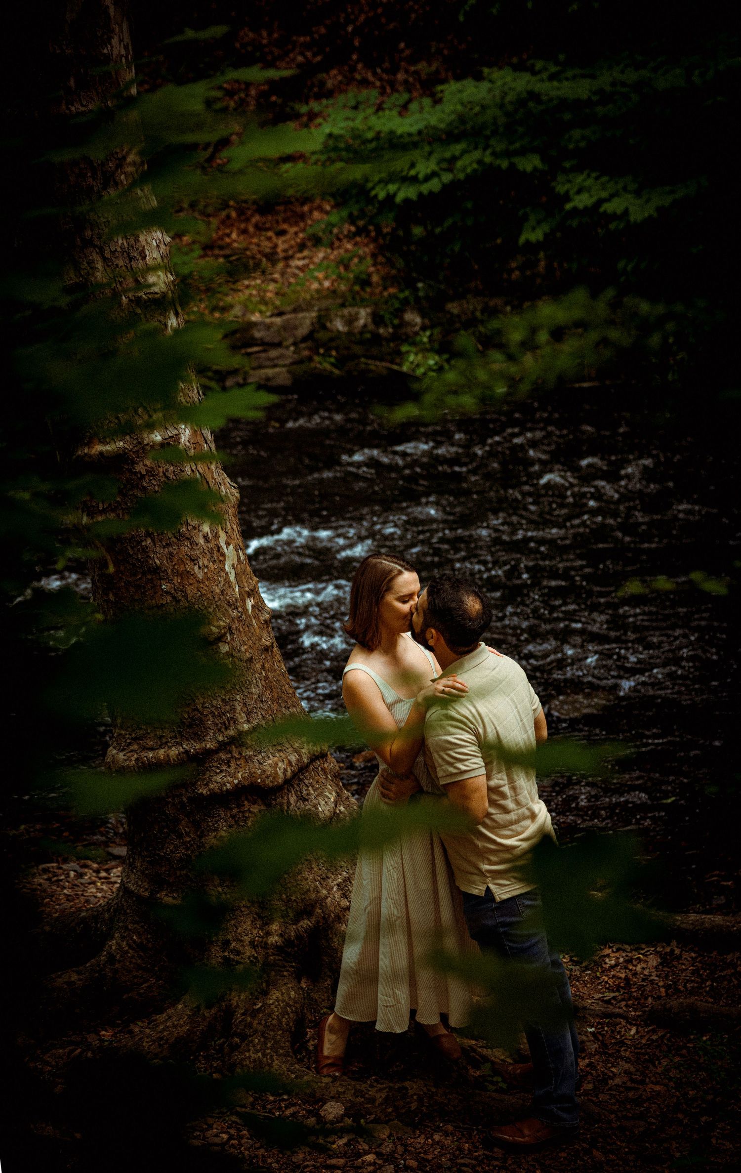 A romantic moment captured by a stream in a lush forest setting with mossy rocks and dappled sunlight. Editorial and Cinematic Wedding photo