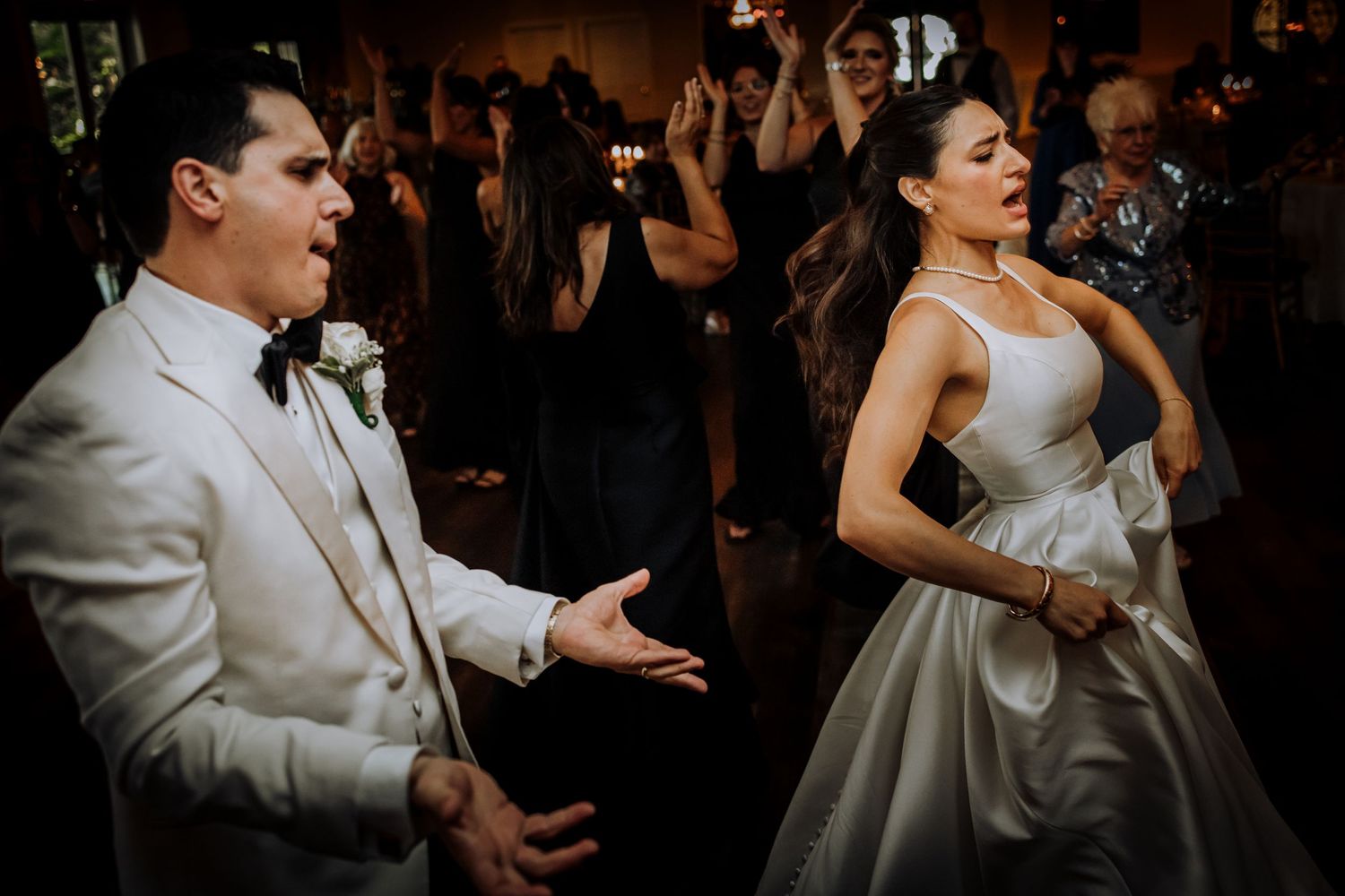 Wedding couple dancing energetically in formal attire during their reception celebration.