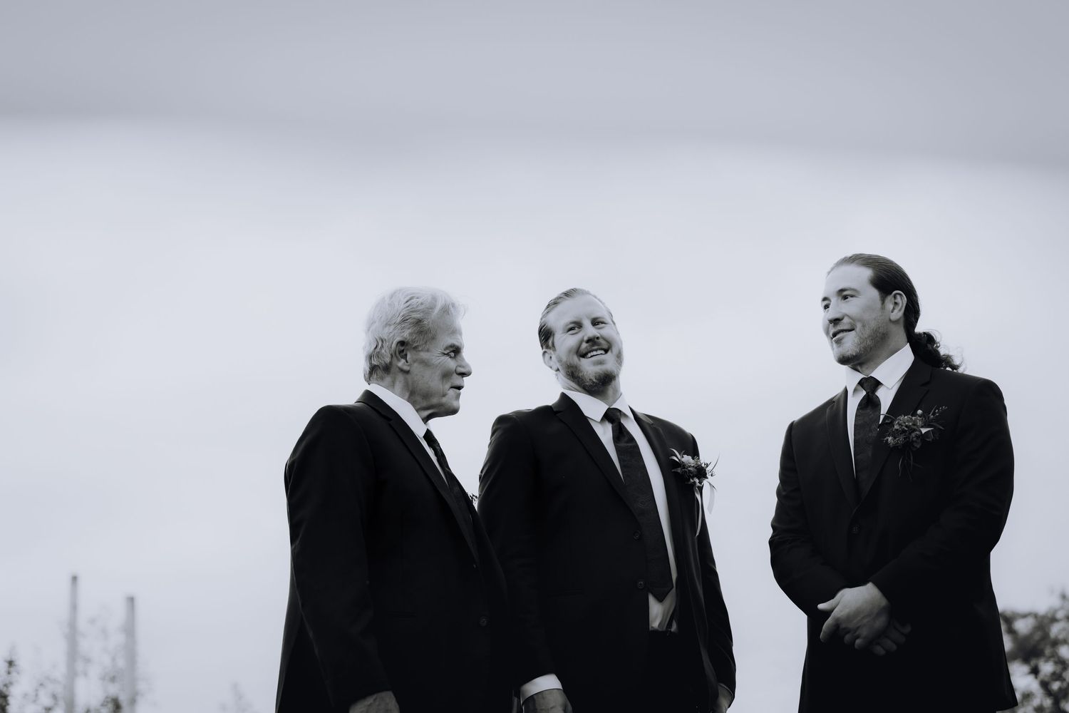 Wedding party members in dark suits stand against a scenic mountain backdrop.