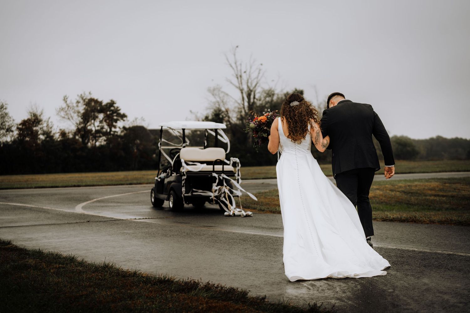 Newlyweds walking towards a vintage car on a rainy wedding day.