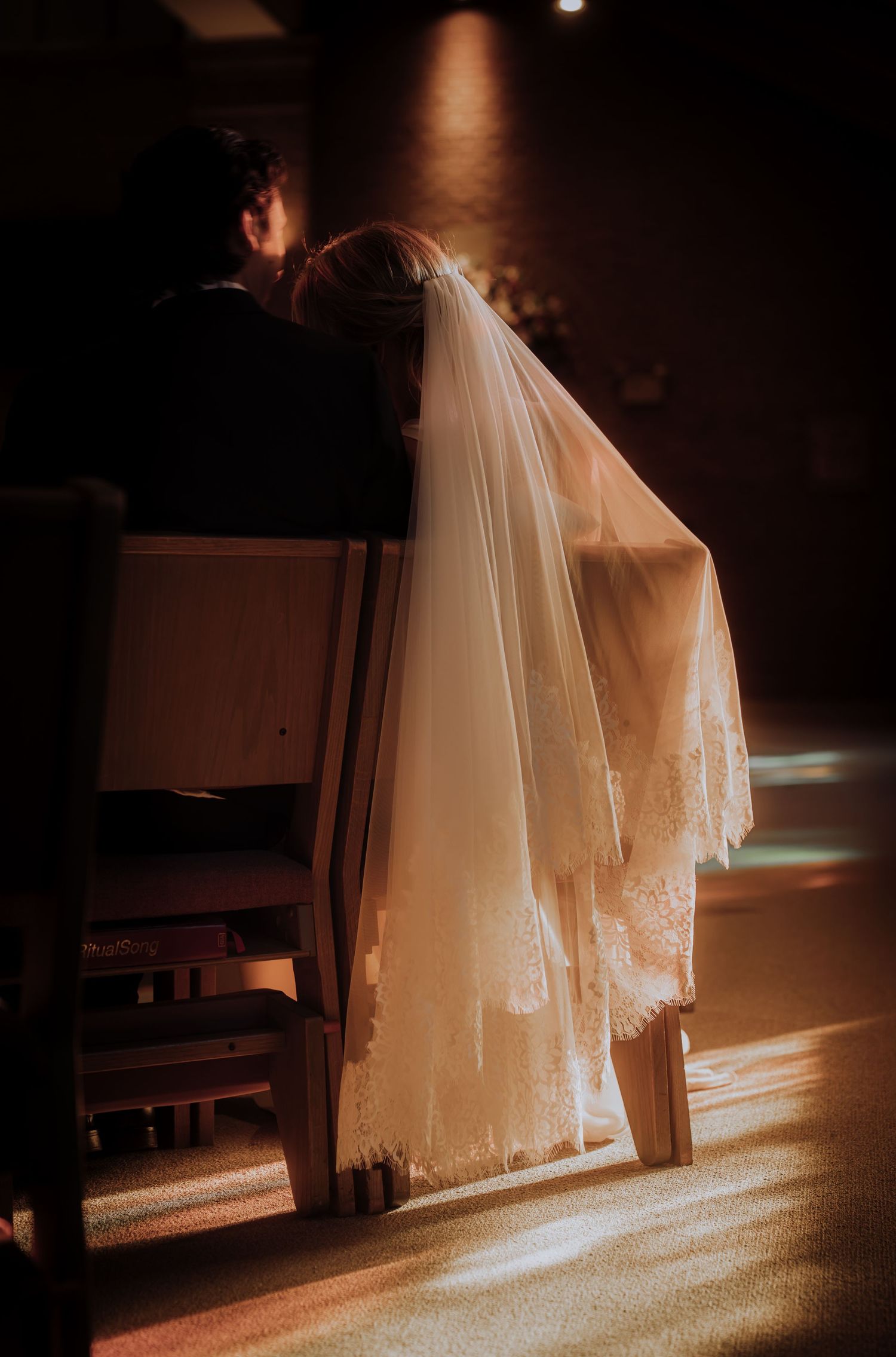 Sunlit wedding veil creates a dreamy silhouette in a dimly lit church setting.