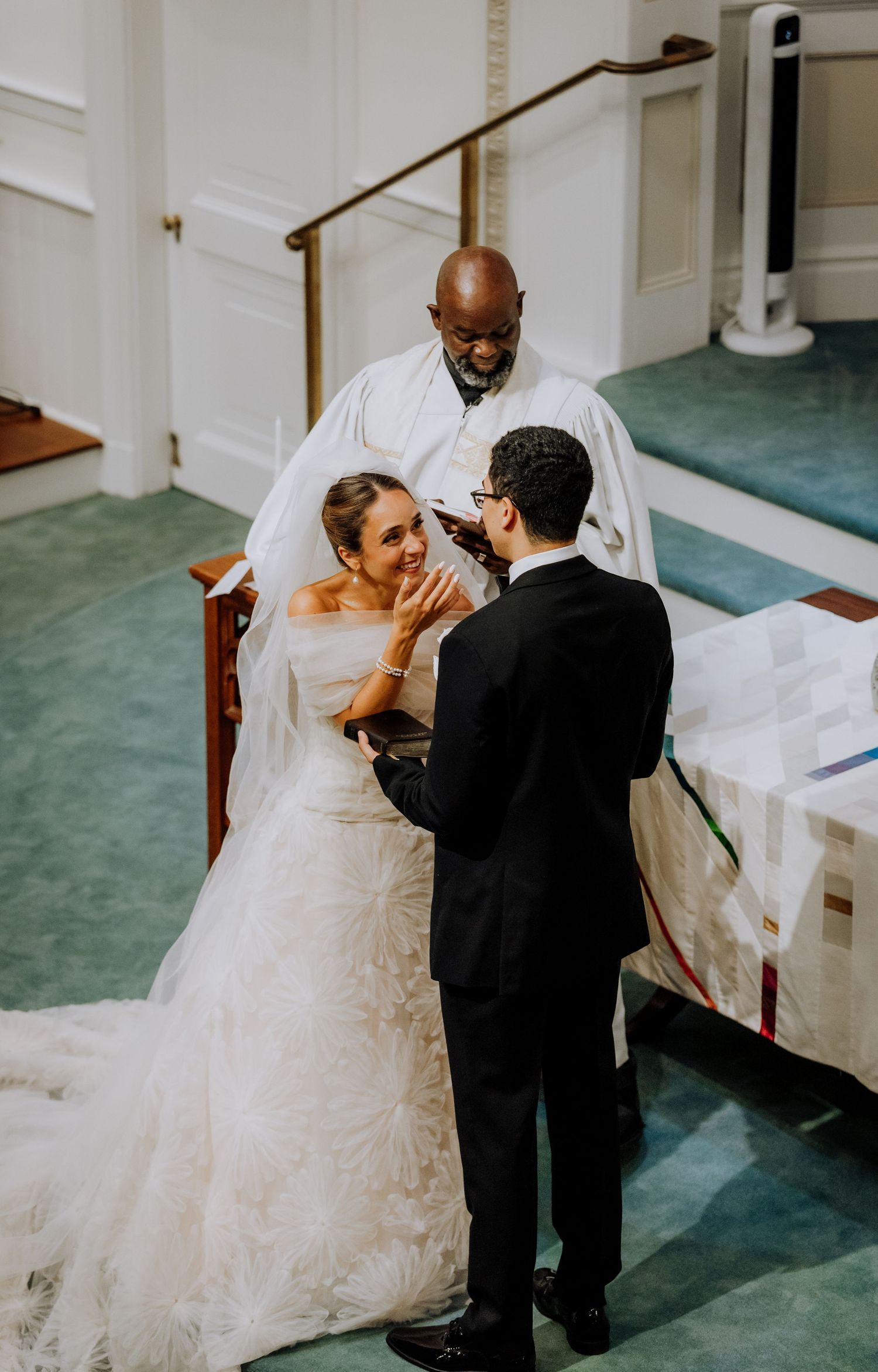 Bride and groom exchange vows at church altar with officiant during elegant wedding ceremony.