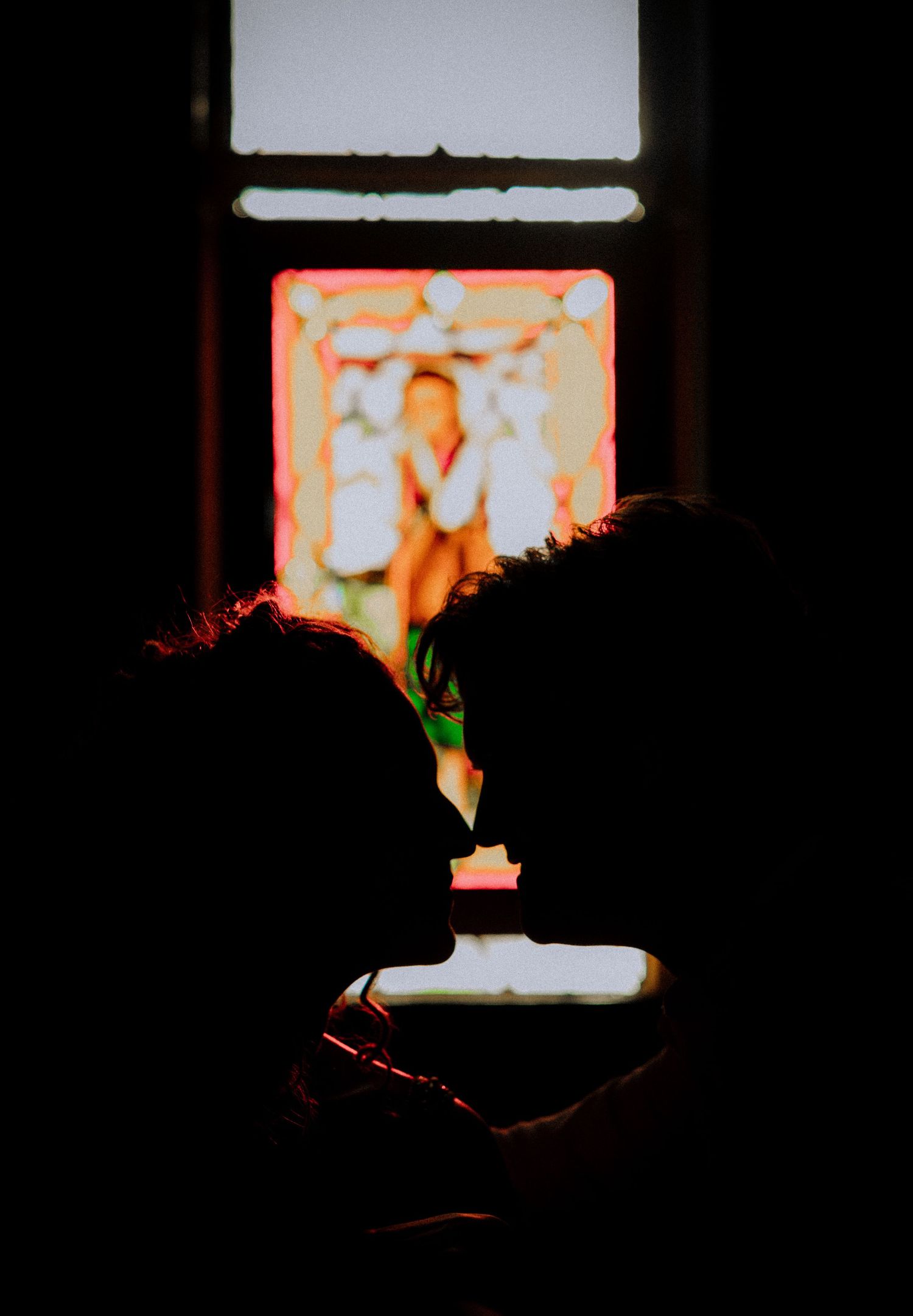 Silhouette of couple against glowing stained glass window in dark church setting.