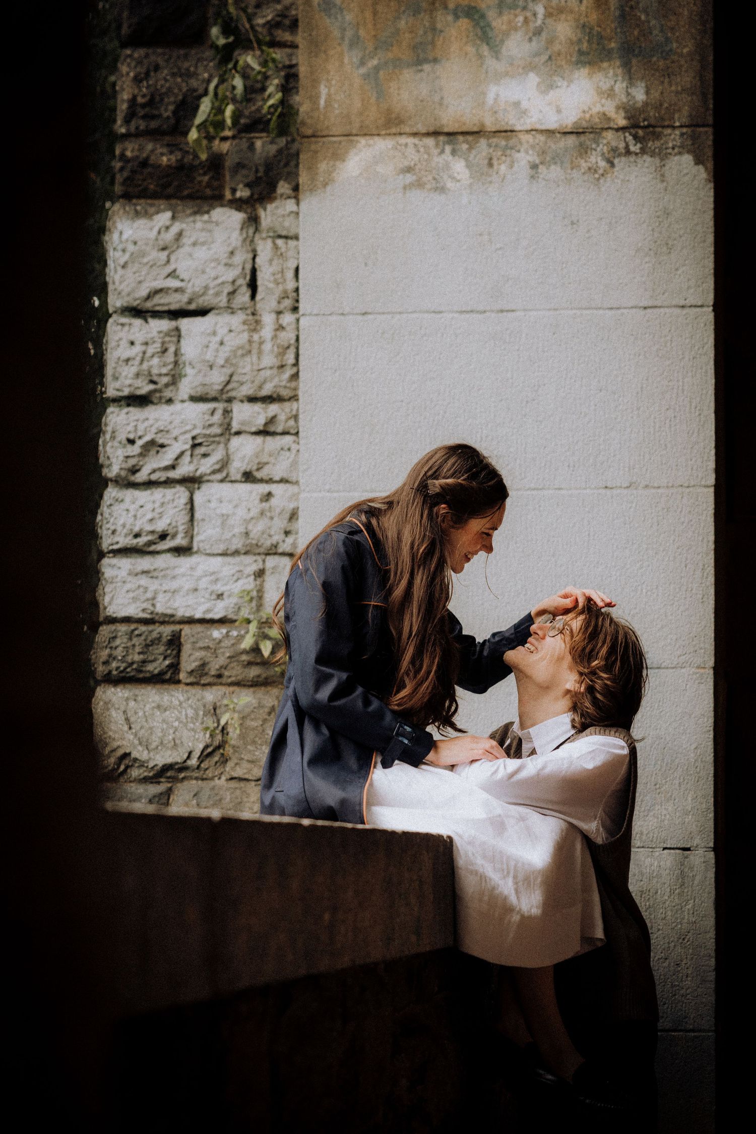 A tender moment captured between two people in a stone archway with natural lighting.