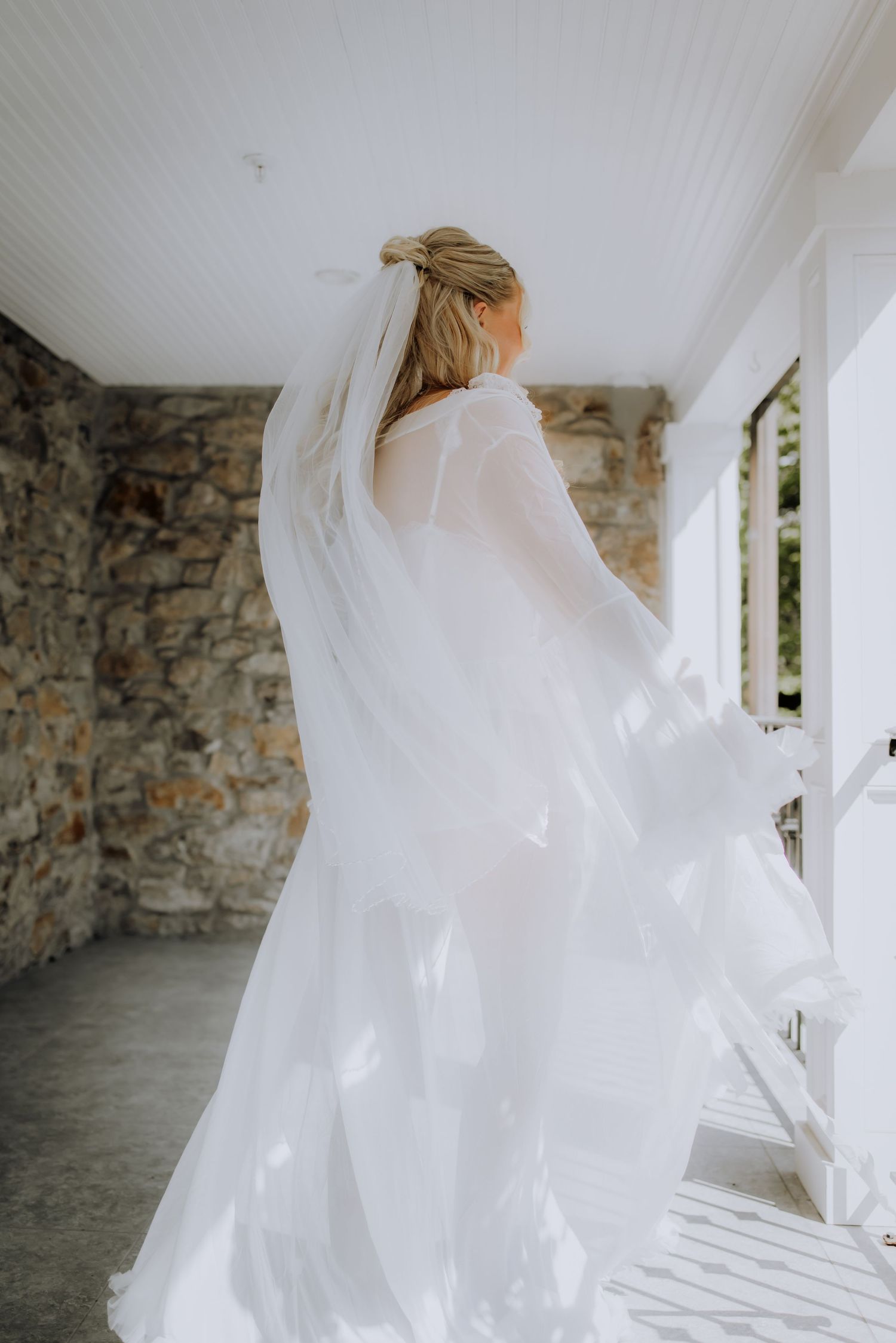 Ethereal bridal veil flowing in breeze against white walls and stone architecture.