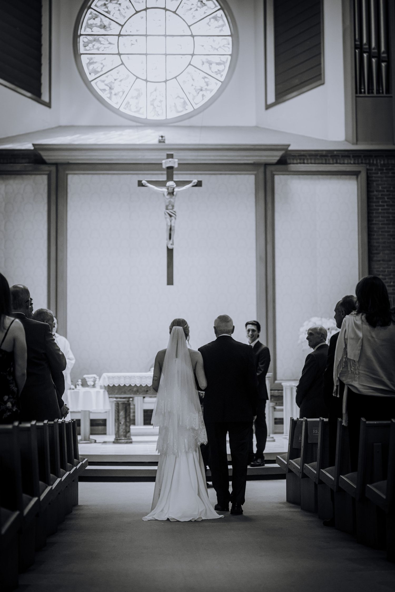 Black and white church wedding ceremony with arched window and cross altar.