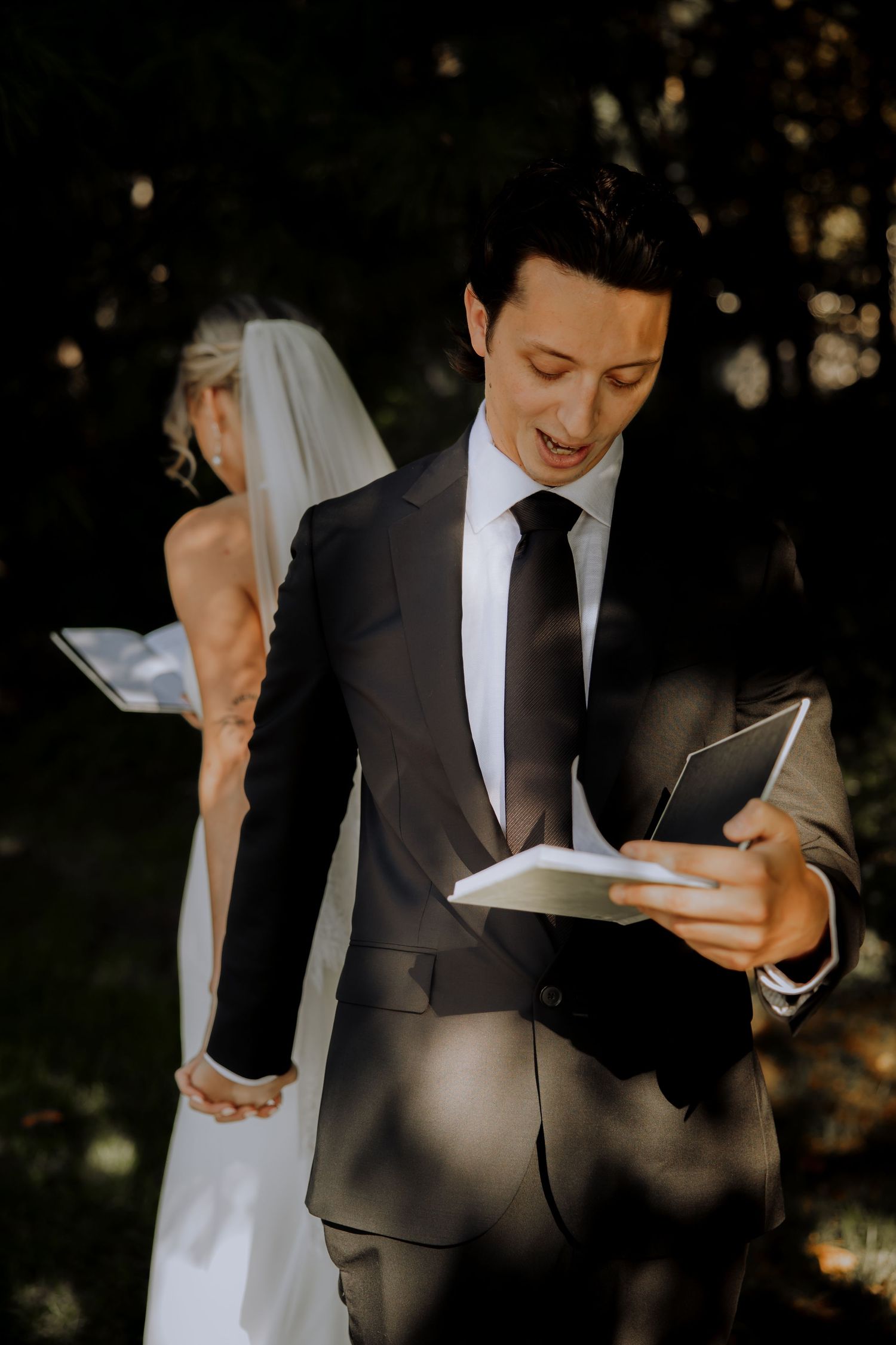 A bride and groom reading vows together during an outdoor ceremony.