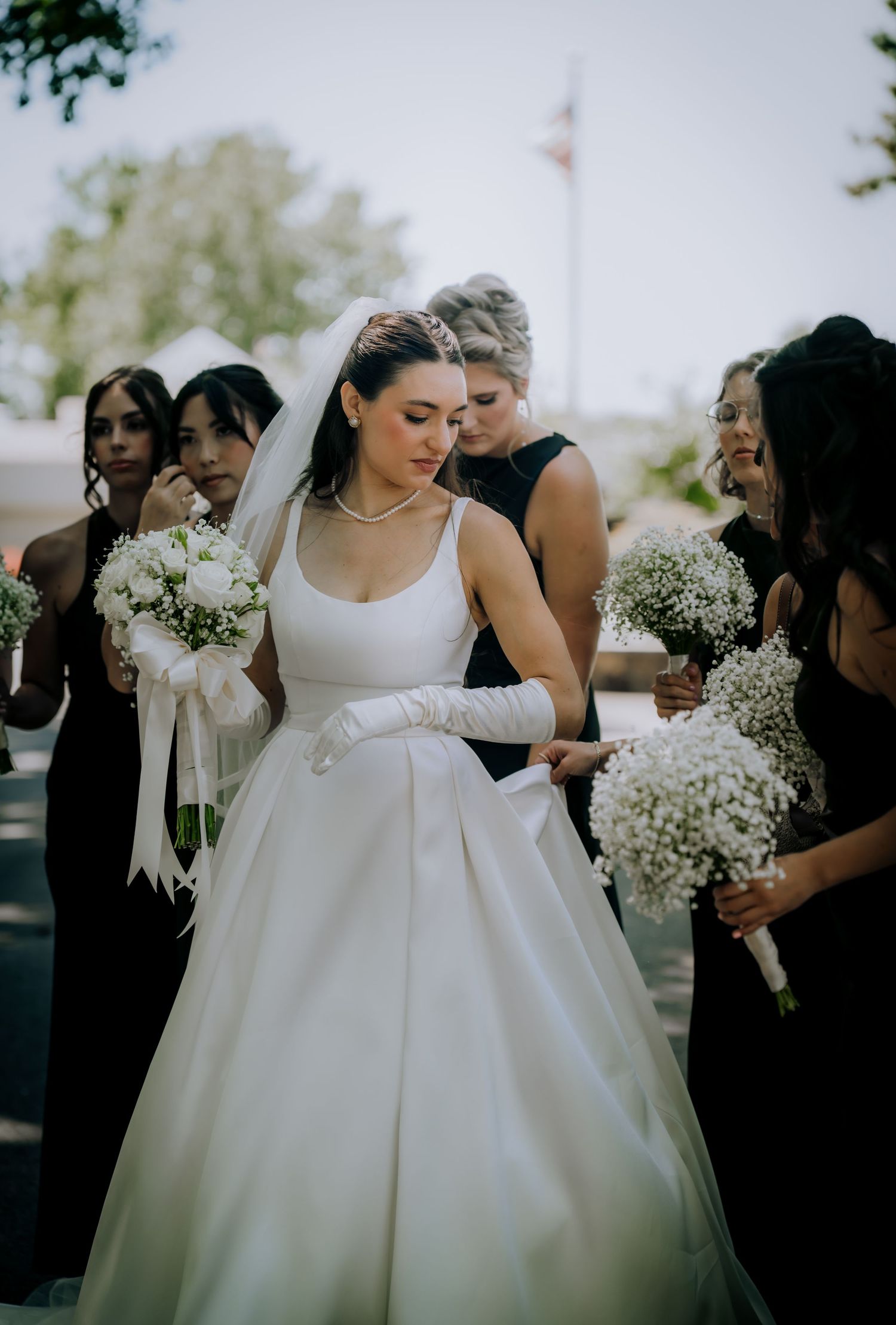 An elegant bride in a classic white ballgown surrounded by bridesmaids in black dresses holding baby's breath bouquets.