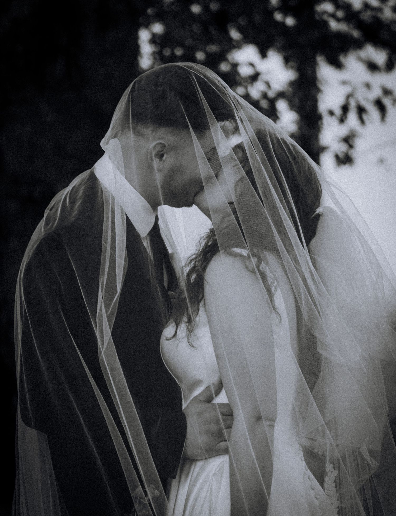 Black and white romantic portrait of newlyweds sharing intimate moment under bridal veil.