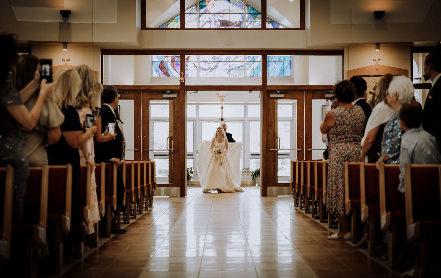 Church pews line both sides of a sunlit aisle leading to stained glass windows at the altar.Editorial and Cinematic Wedding photos