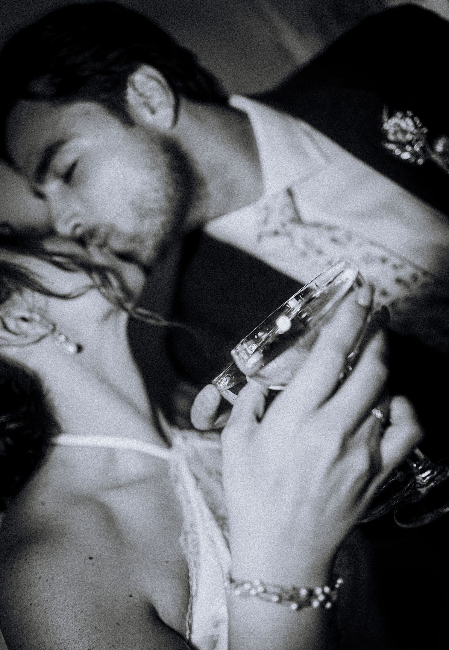 Black and white photo of a couple sharing a romantic kiss, woman holding a champagne glass with bracelet.