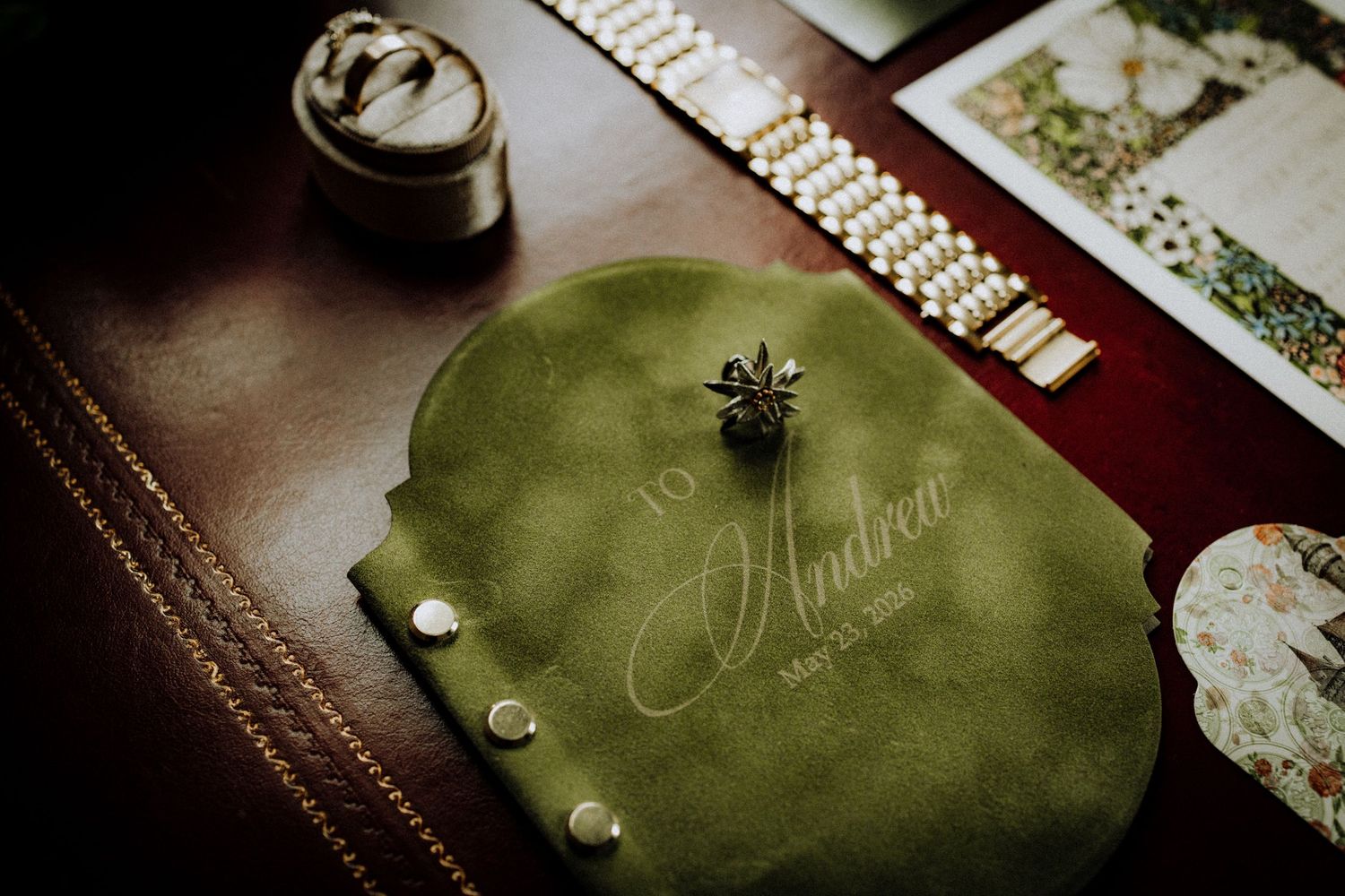 Green velvet jewelry pouch personalized with Andrea name and date, displayed on dark leather surface with pearl bracelet.