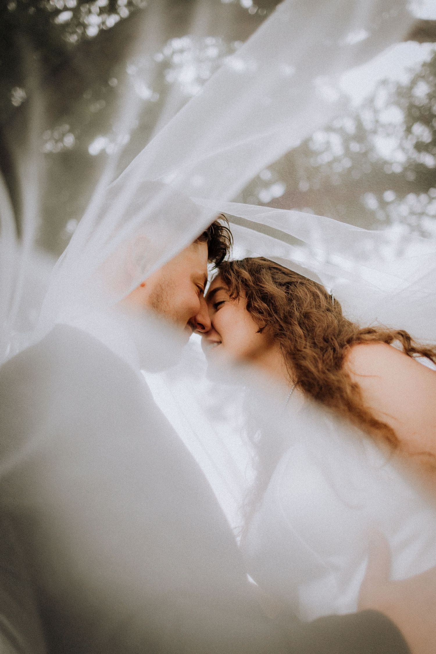 Ethereal wedding portrait through flowing white veil creating dreamy effect.