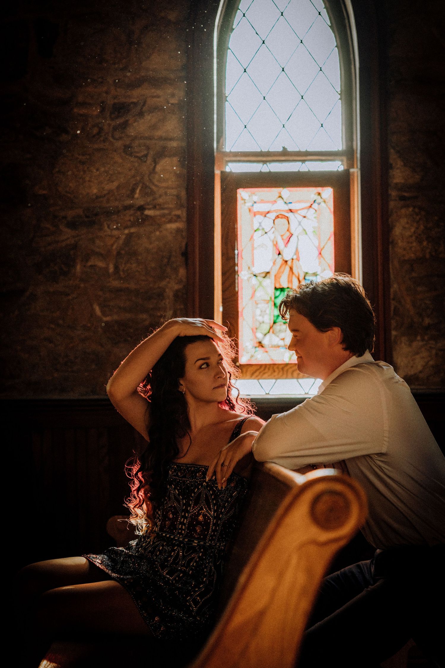 Romantic couple sharing an intimate moment in front of a stained glass window in a historic church.