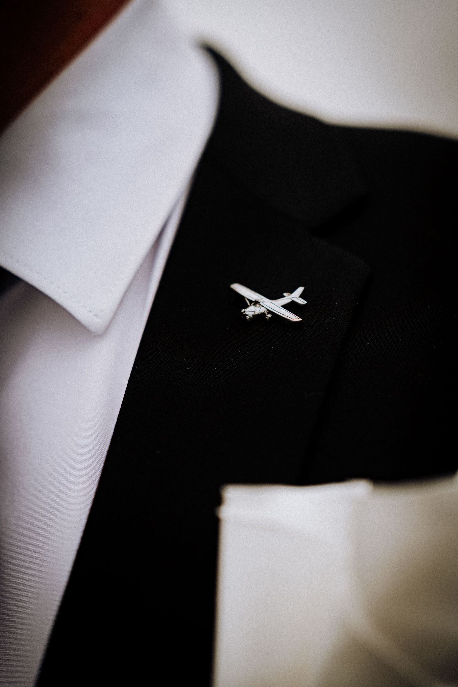 A close-up of an airplane pin on a black suit lapel.