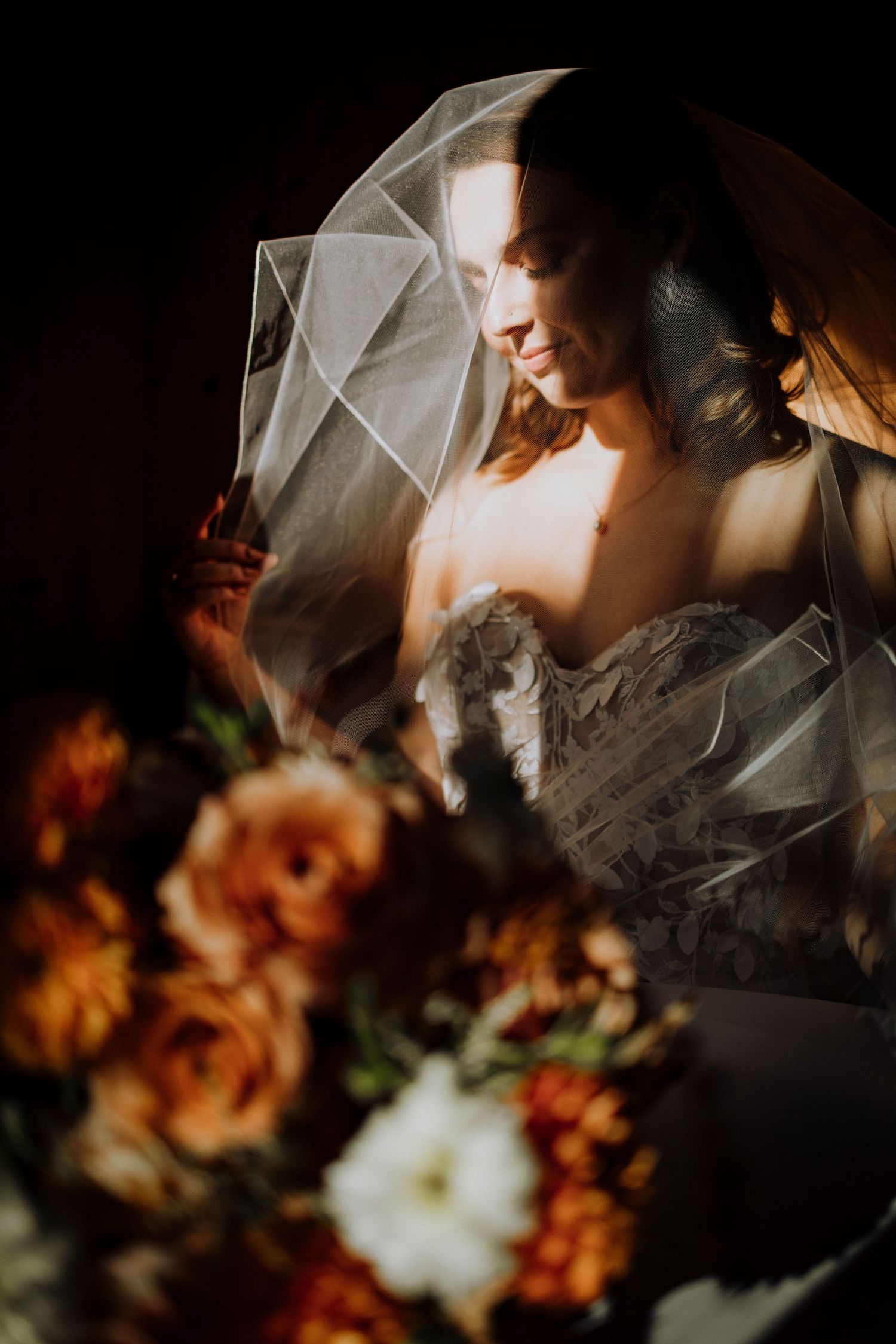 Dramatic side lighting illuminates a bridal portrait with autumn-colored flowers in the foreground.