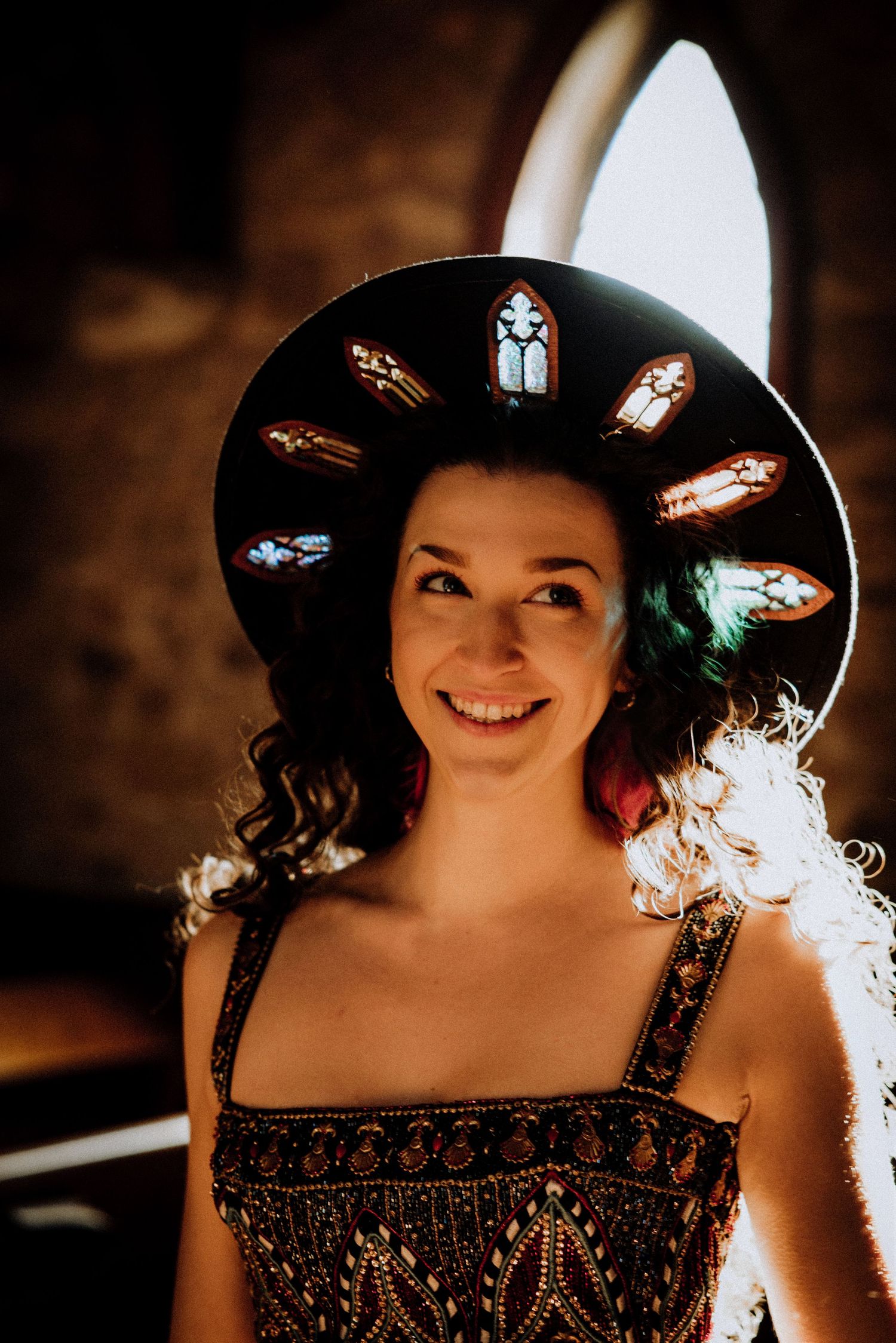 Woman wearing decorative halo-style headpiece with stained glass designs in church setting.