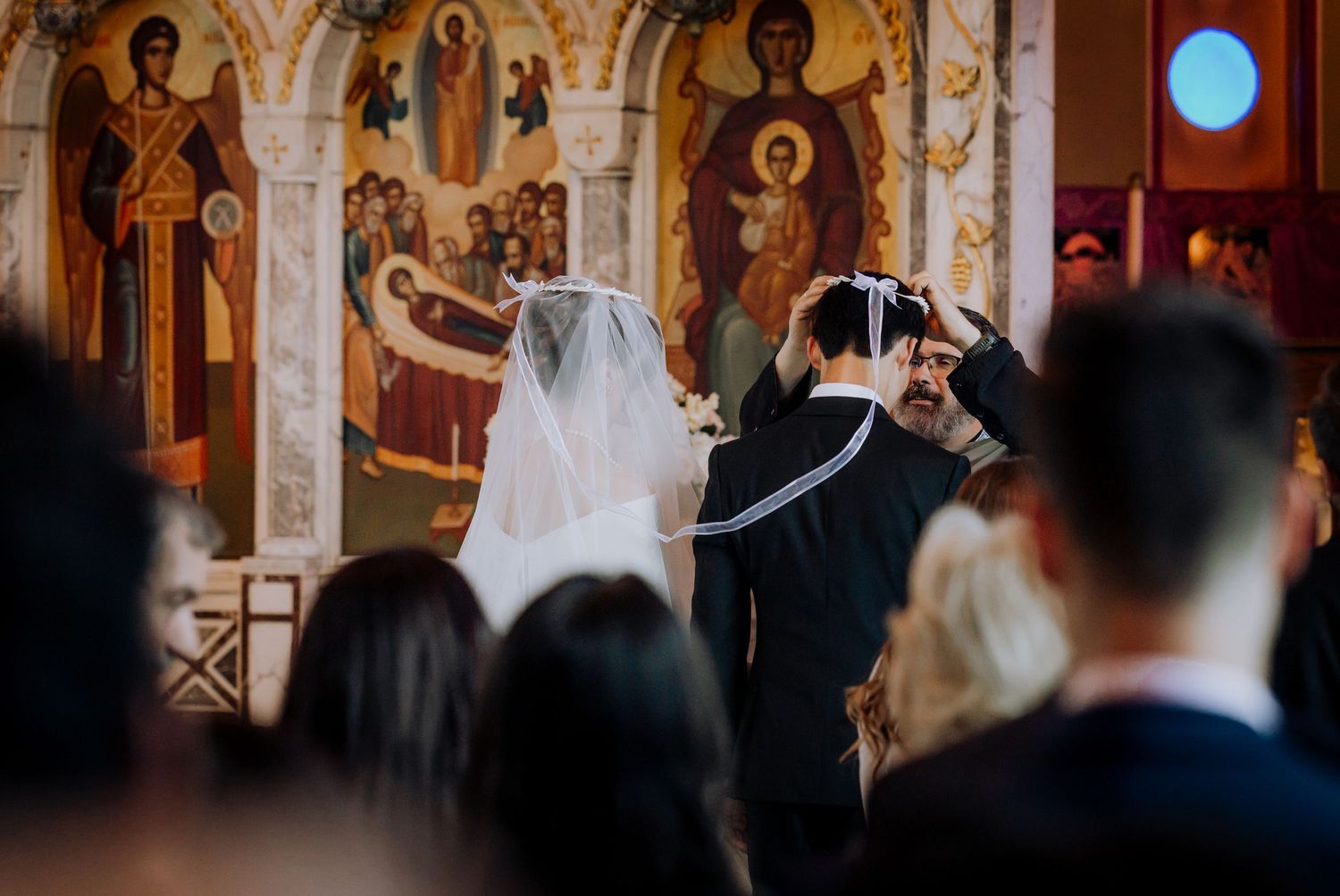 Orthodox wedding ceremony with bride and groom before ornate Byzantine church icons and frescoes.