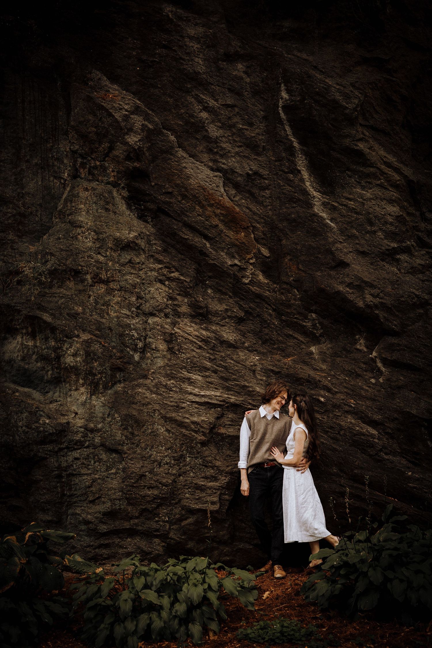 Couple in white clothing dancing against dramatic rocky cliff backdrop.