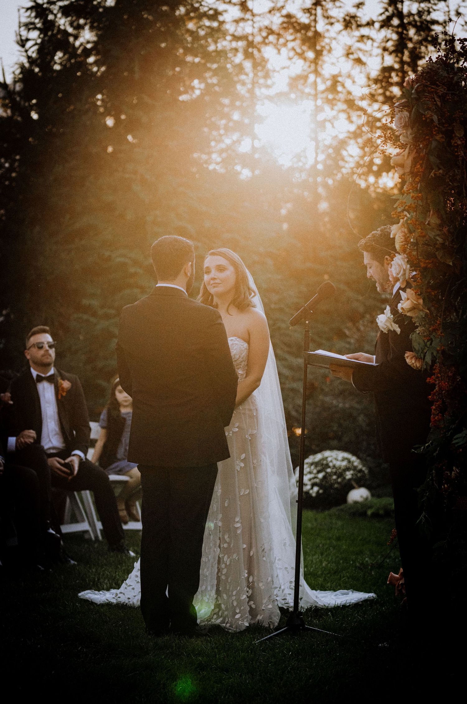 Wedding ceremony in a garden setting during golden hour with guests watching.