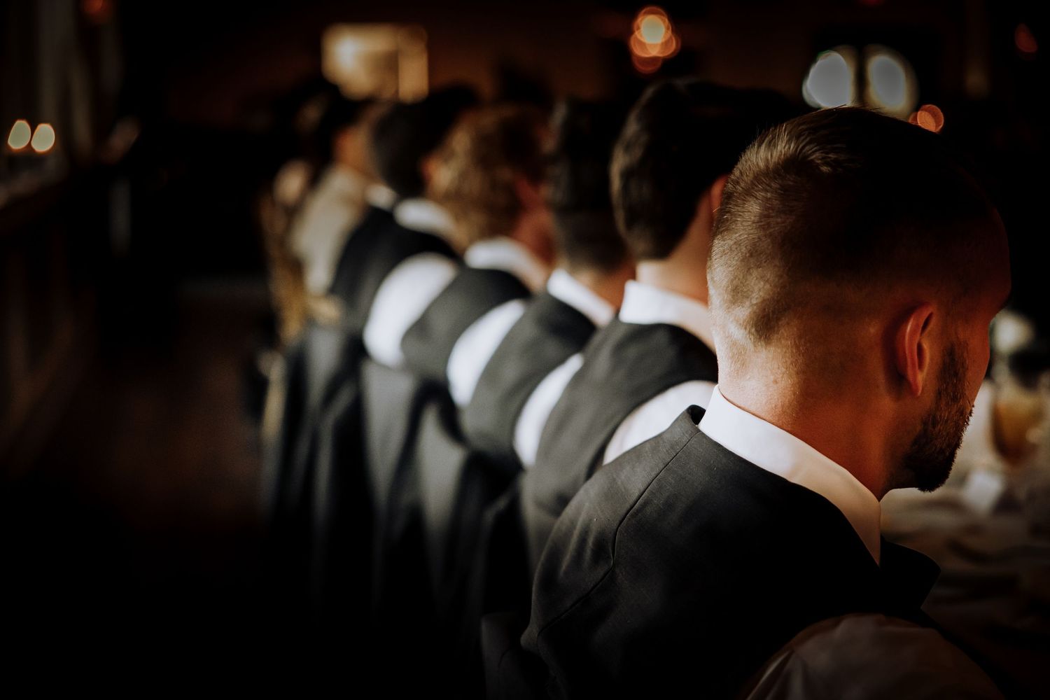 Row of groomsmen in dark suits standing at wedding ceremony.